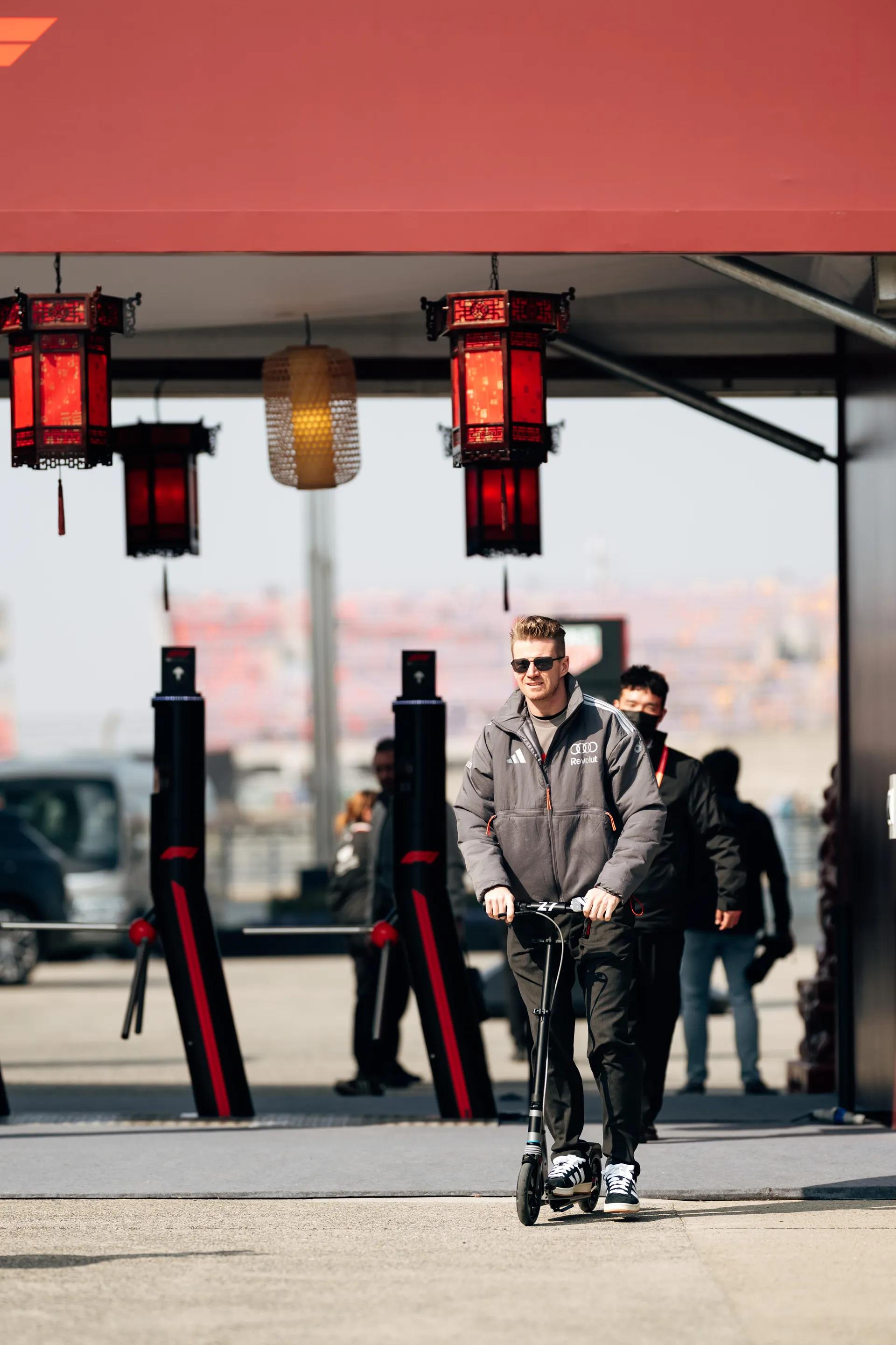 Nico Hulkenberg rides a scooter through the Shanghai paddock beneath red lanterns during the Chinese Grand Prix weekend.