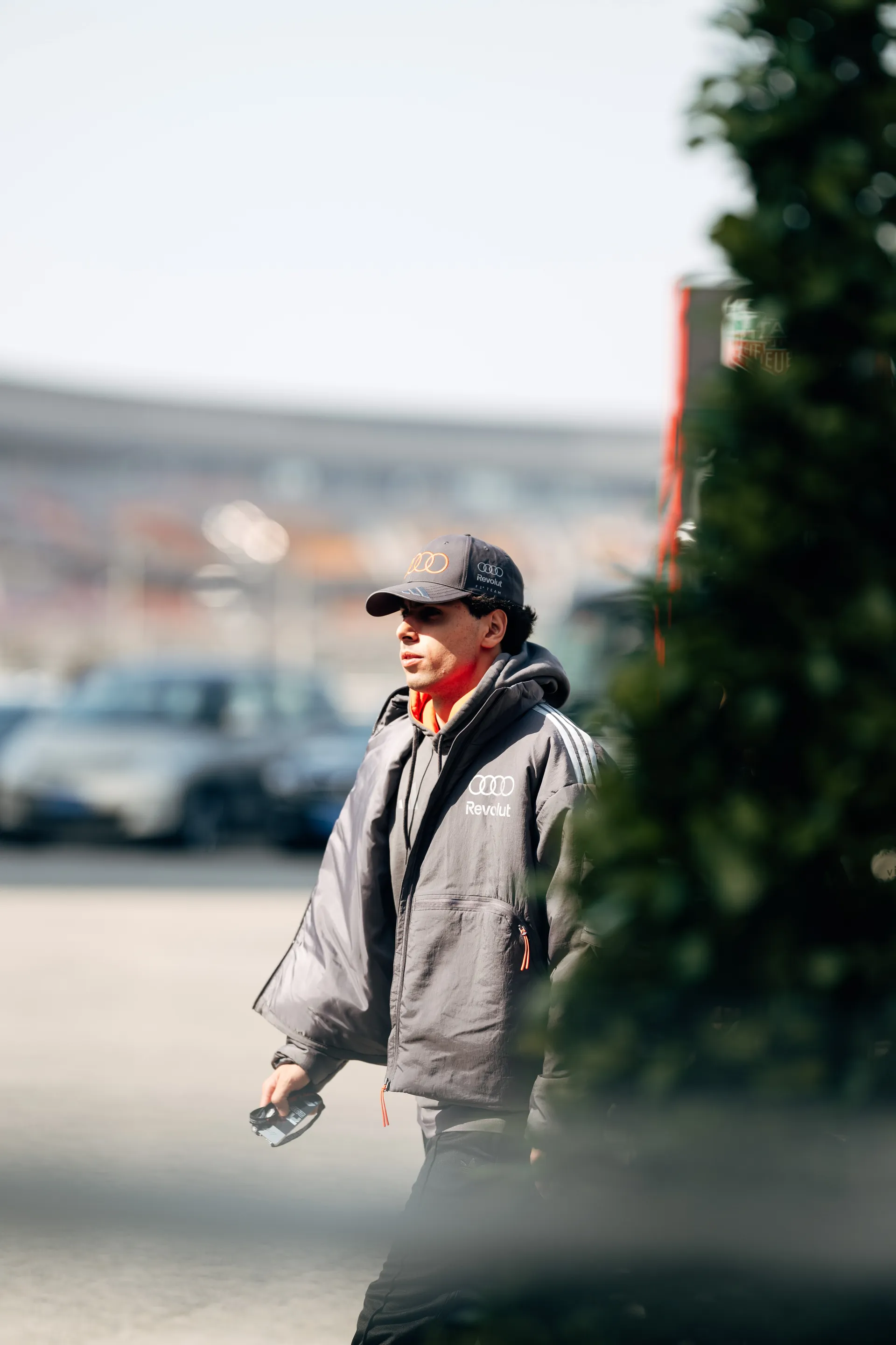 Gabriel Bortoleto walks through the Shanghai paddock in Audi Revolut F1® Team gear, partially framed by greenery.