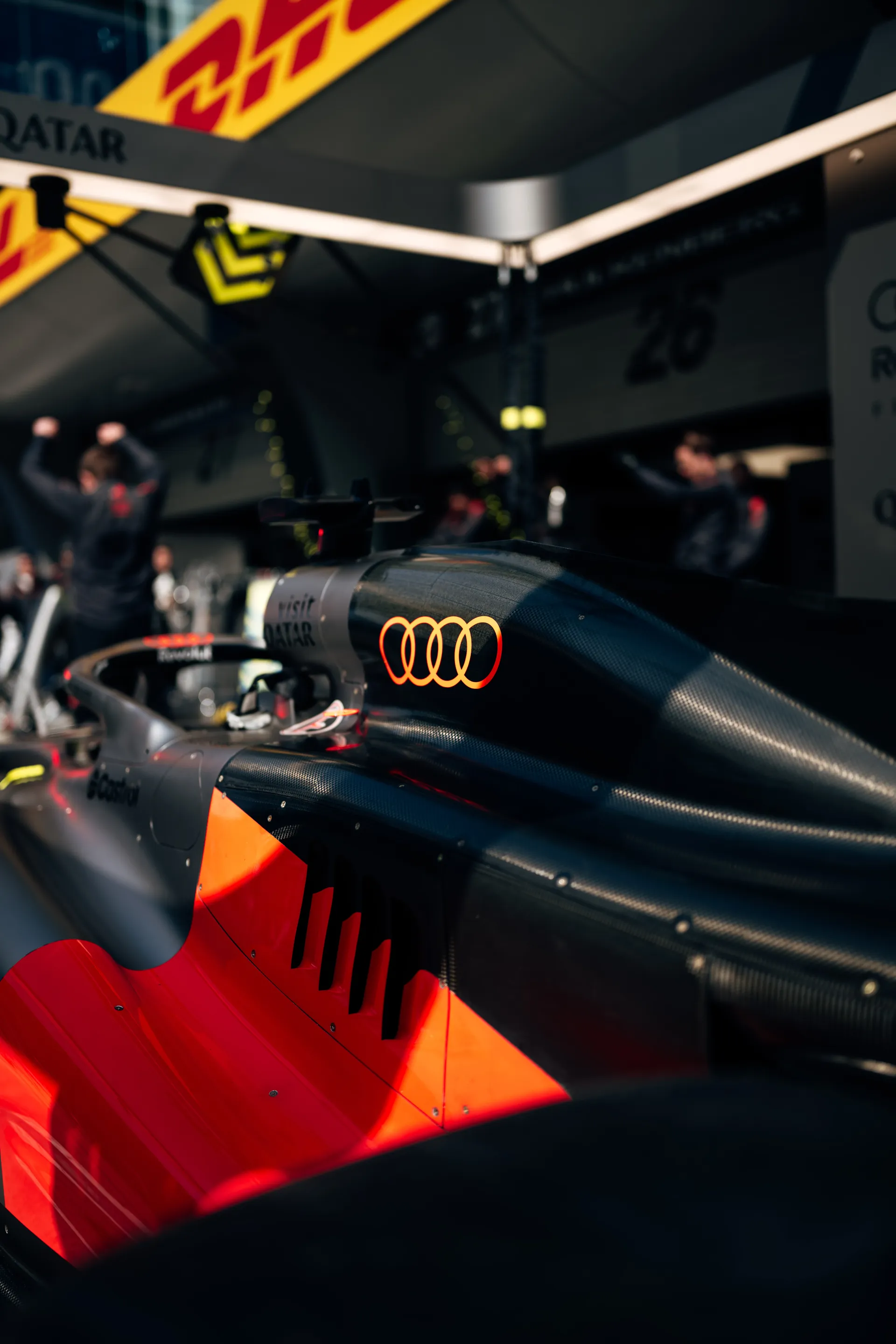 Close up of the Audi Revolut F1® Team race car in the Shanghai garage, with bright Audi rings on the bodywork and team activity blurred in the background.