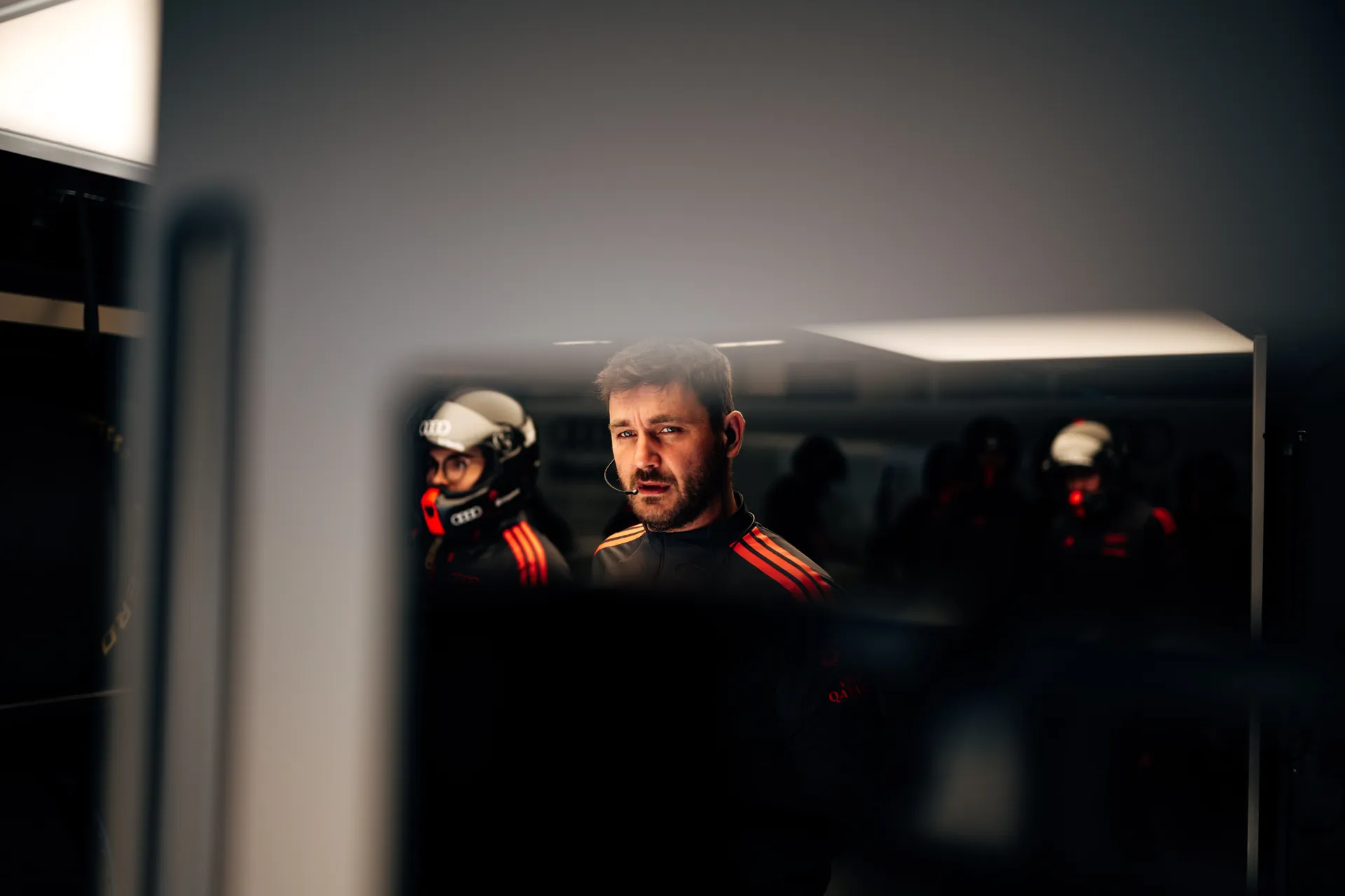 Audi Revolut F1® Team crew member stands inside the garage in Shanghai, framed by reflections and helmeted colleagues in the background.