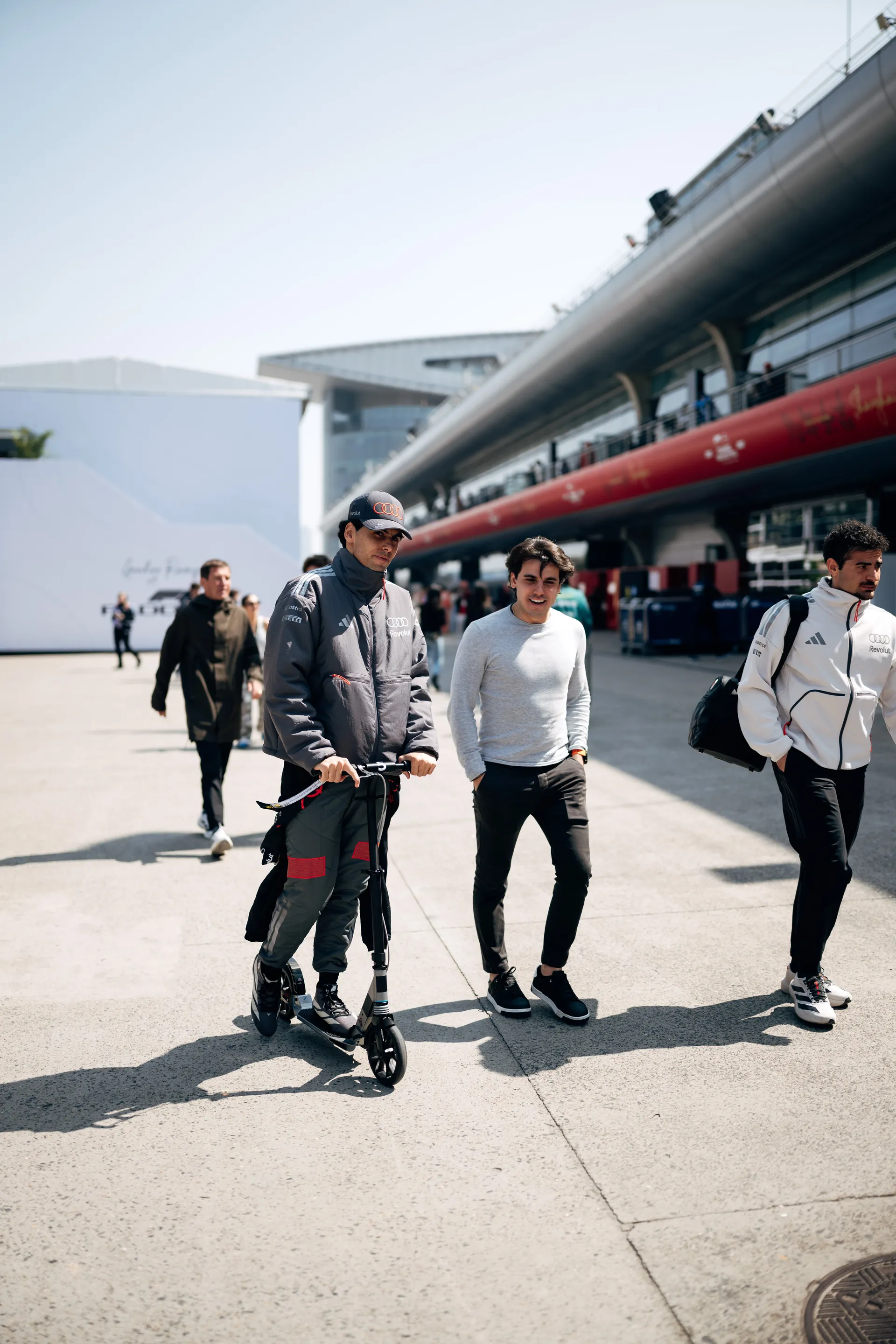 Gabriel Bortoleto rides a scooter through the Shanghai paddock with Audi Revolut F1® Team members walking alongside him.