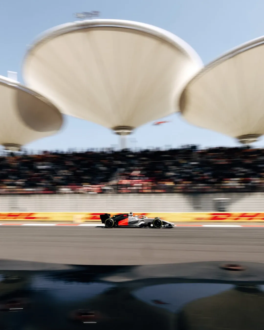 Audi Revolut F1® Team car speeds through Shanghai, framed by the circuit grandstands and distinctive roof structures.