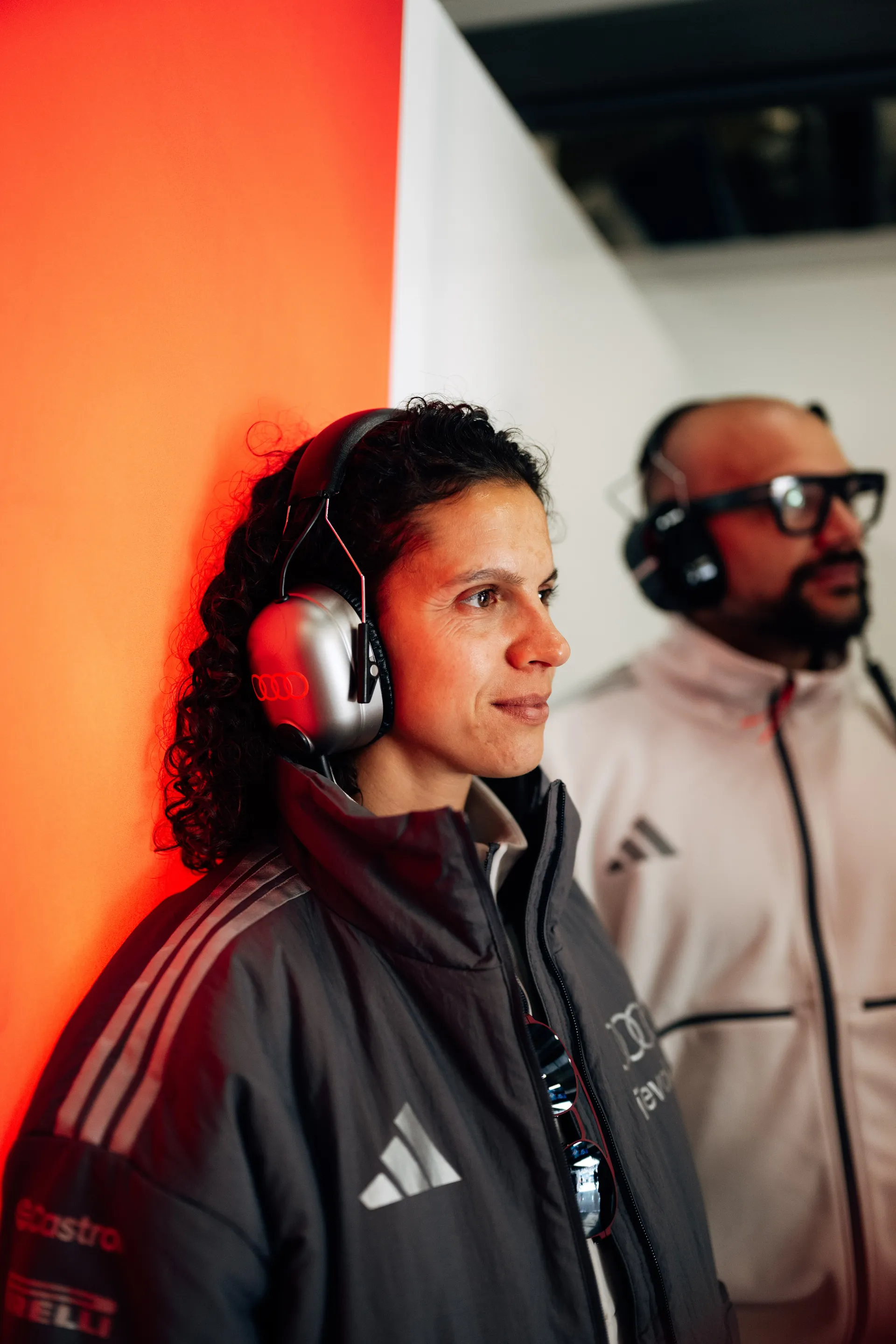 Audi Revolut F1® Team team member wearing a headset watches track activity from the Shanghai garage, with warm red light in the background.