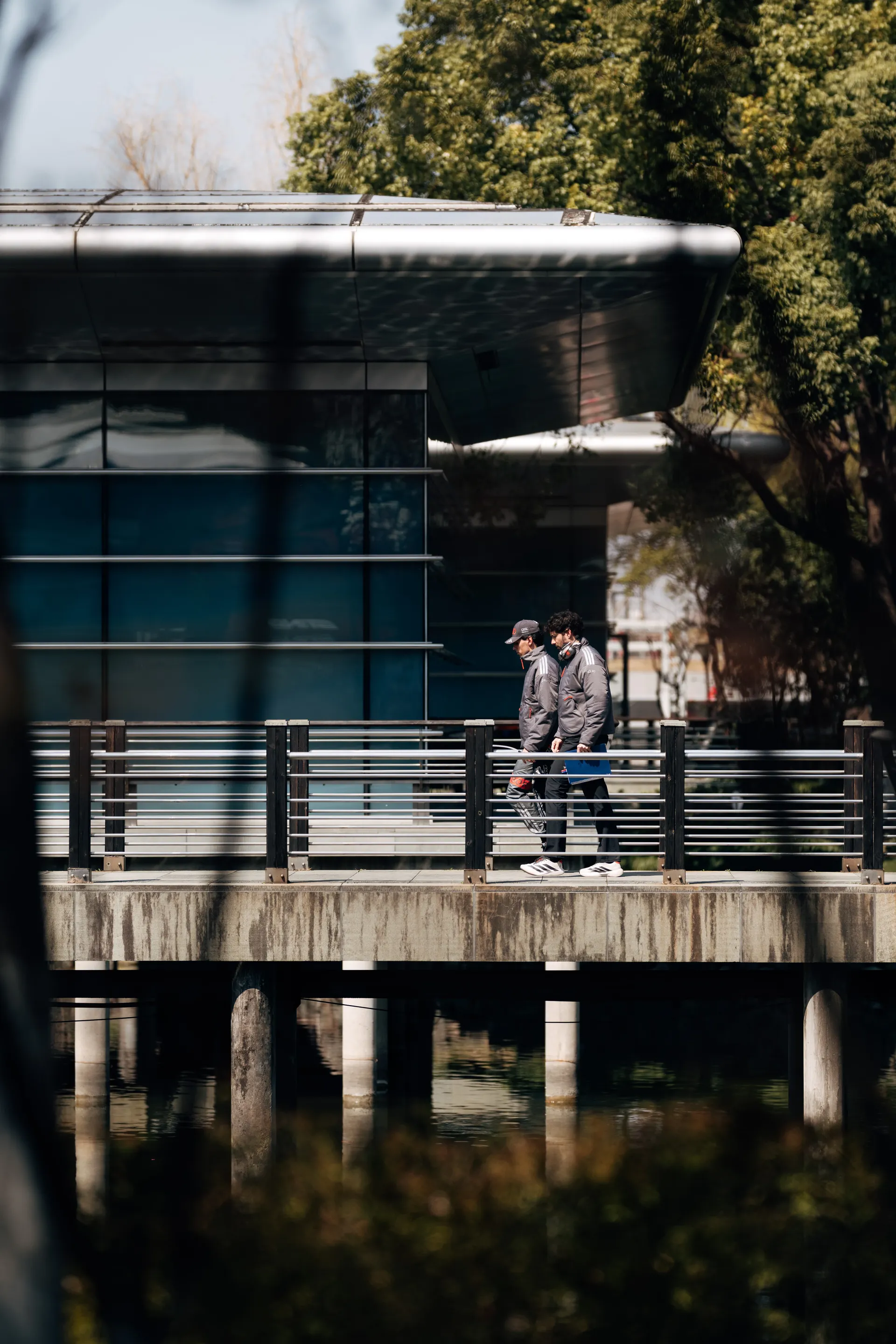 Two Audi Revolut F1® Team member and Gabriel Bortoleto walk across a bridge in the Shanghai paddock beside the water.
