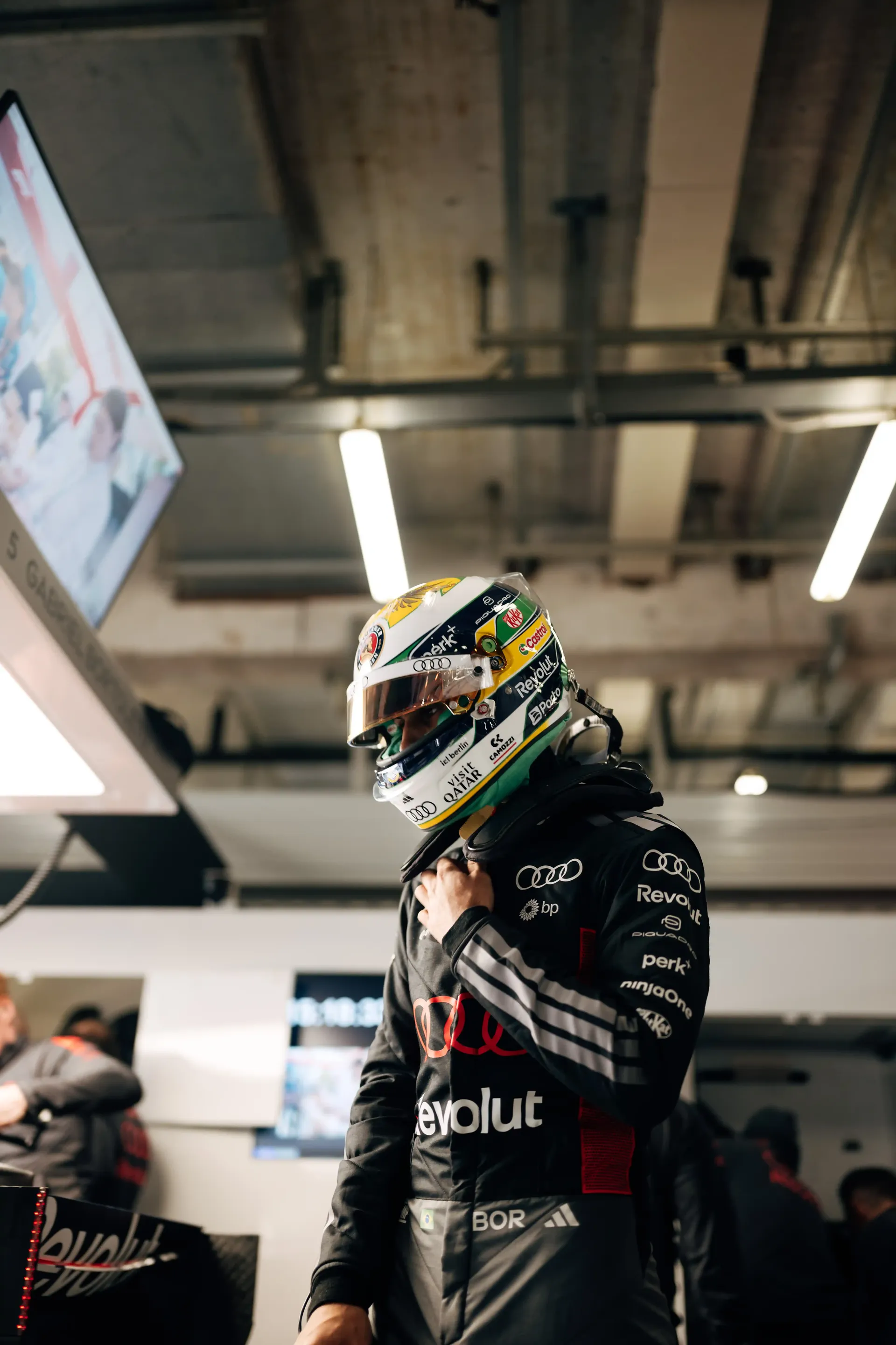 Audi Revolut F1® Team driver Gabriel Bortoleto standing in the pit garage wearing full racing suit and helmet.