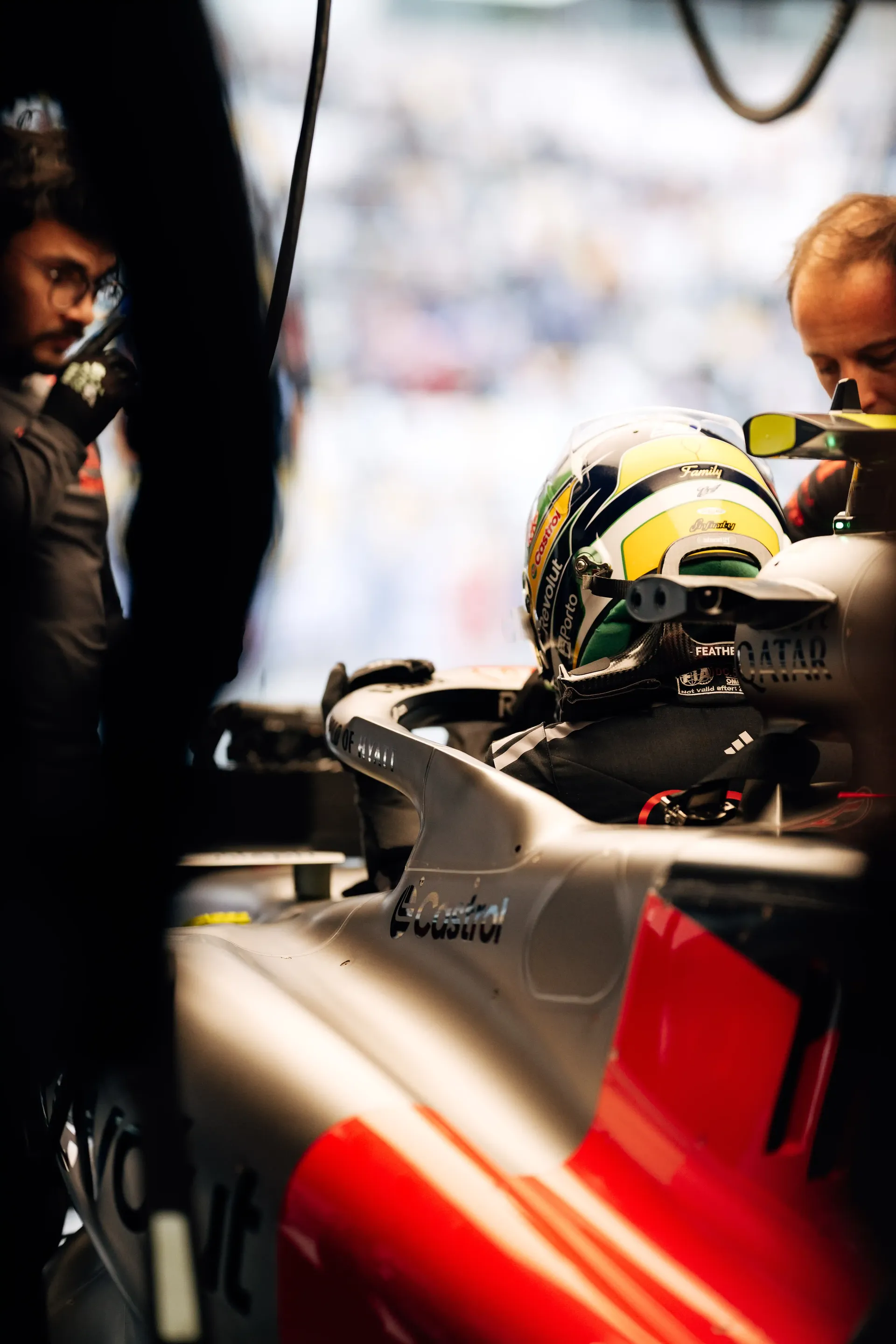 Audi Revolut F1® Team driver Gabriel Bortoleto seated in the race car cockpit while mechanics prepare the car in the garage.