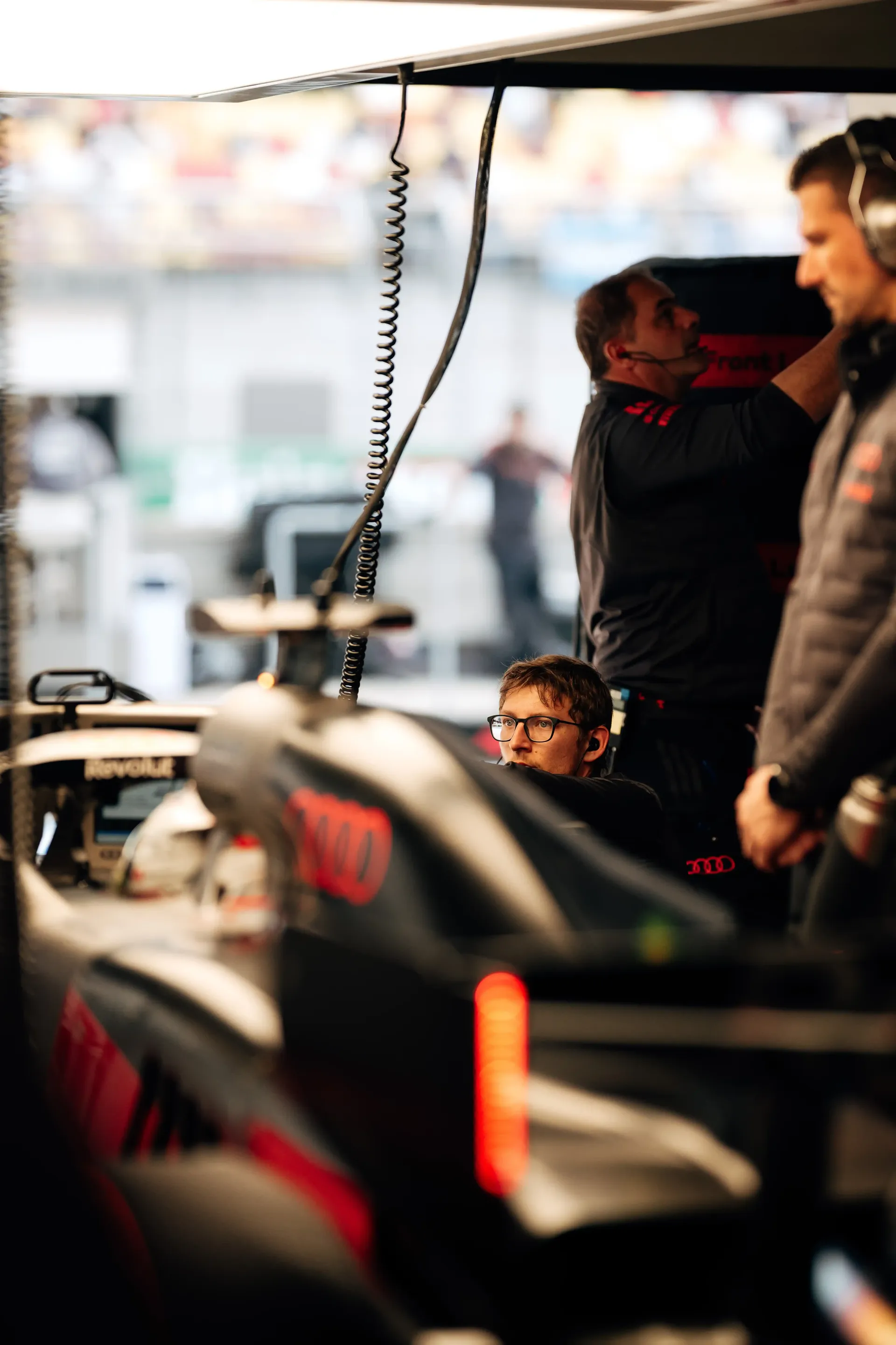 Audi Revolut F1® Team pit crew members working around the race car during garage preparations.