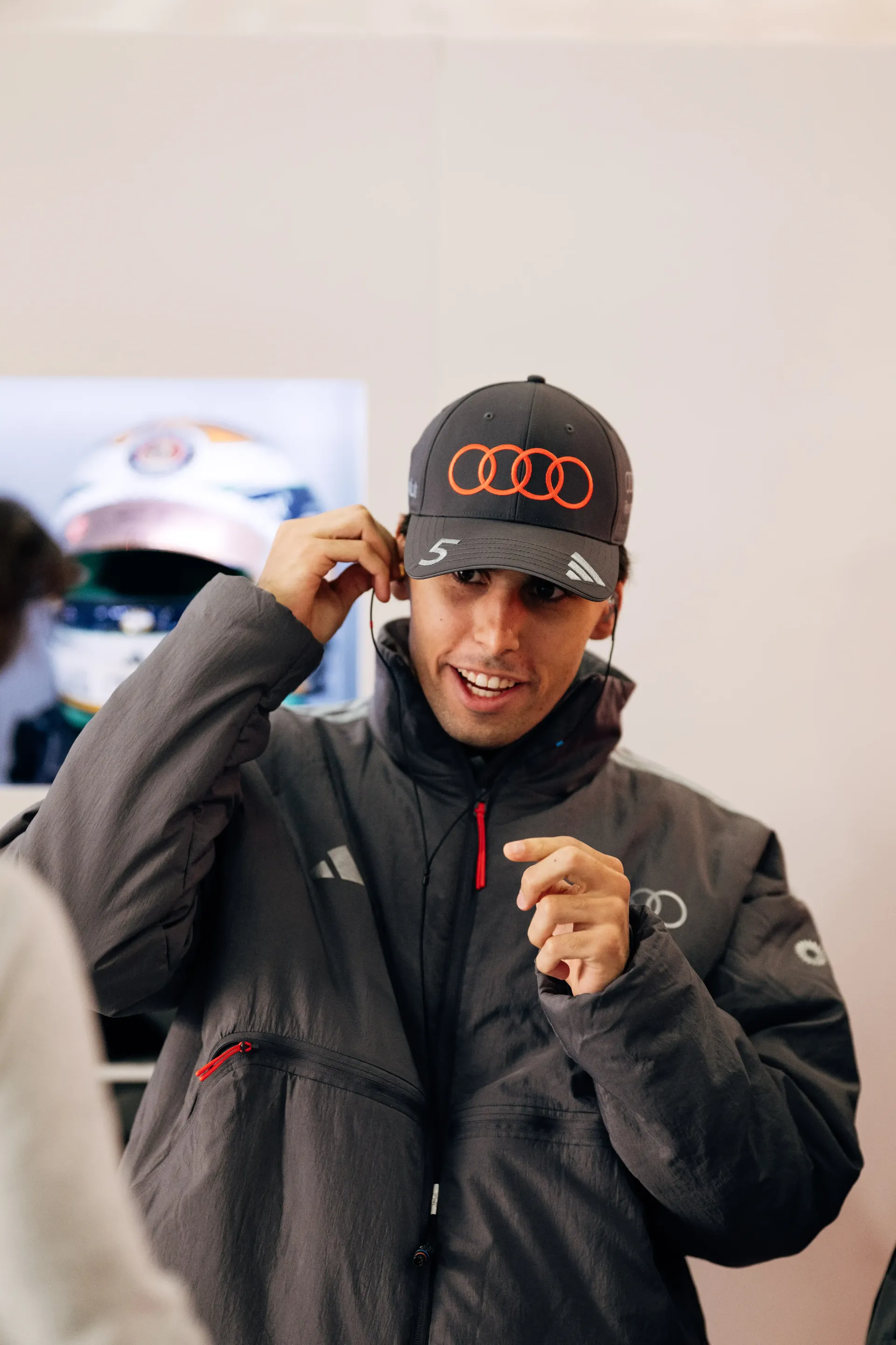 Audi Revolut F1® Team driver Gabriel Bortoleto smiling while listening to music and standing inside the garage of the racetrack