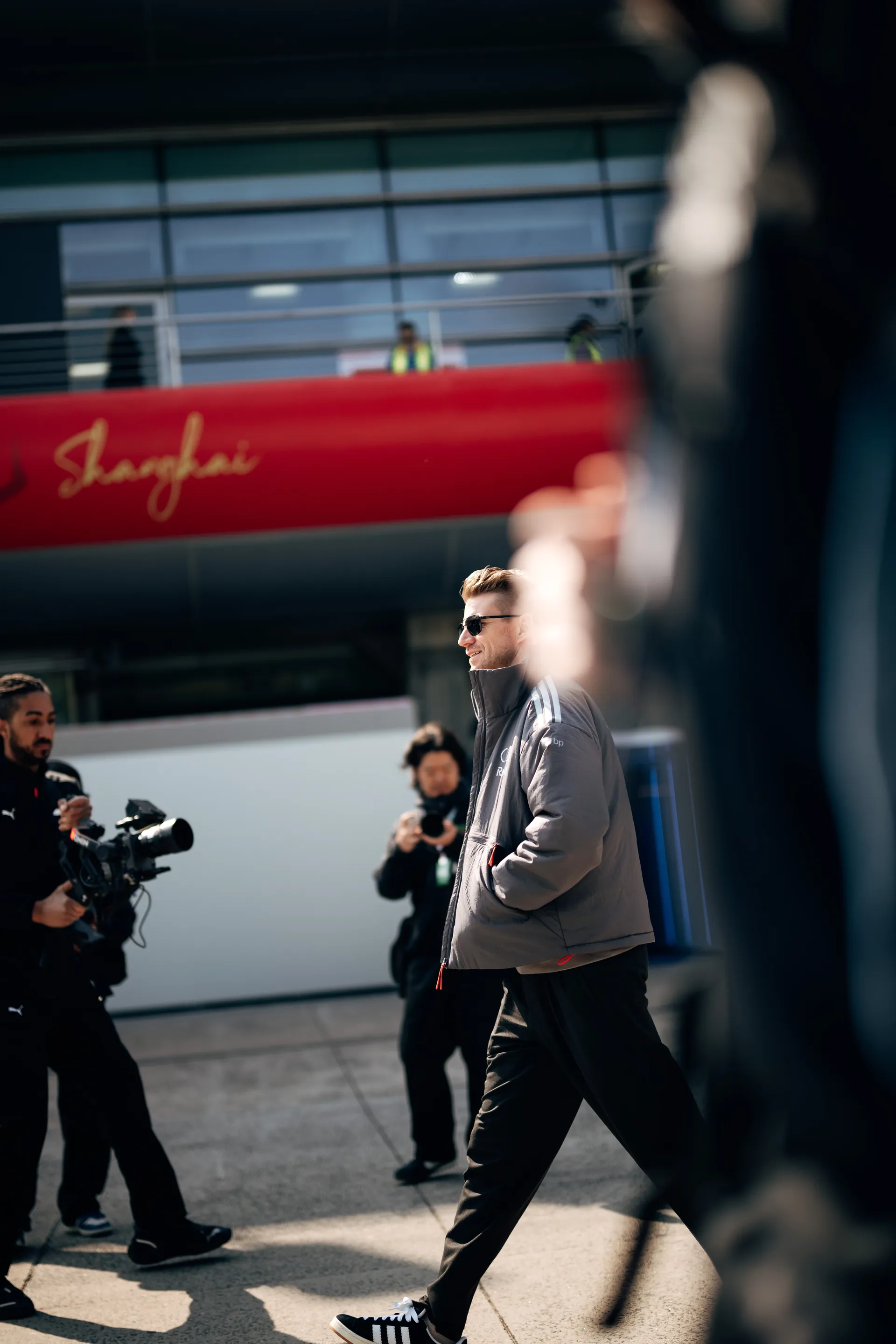 An Audi Revolut F1® Team driver Nico Hulkenberg walks through the paddock in Shanghai as camera crew and team activity unfold around him.