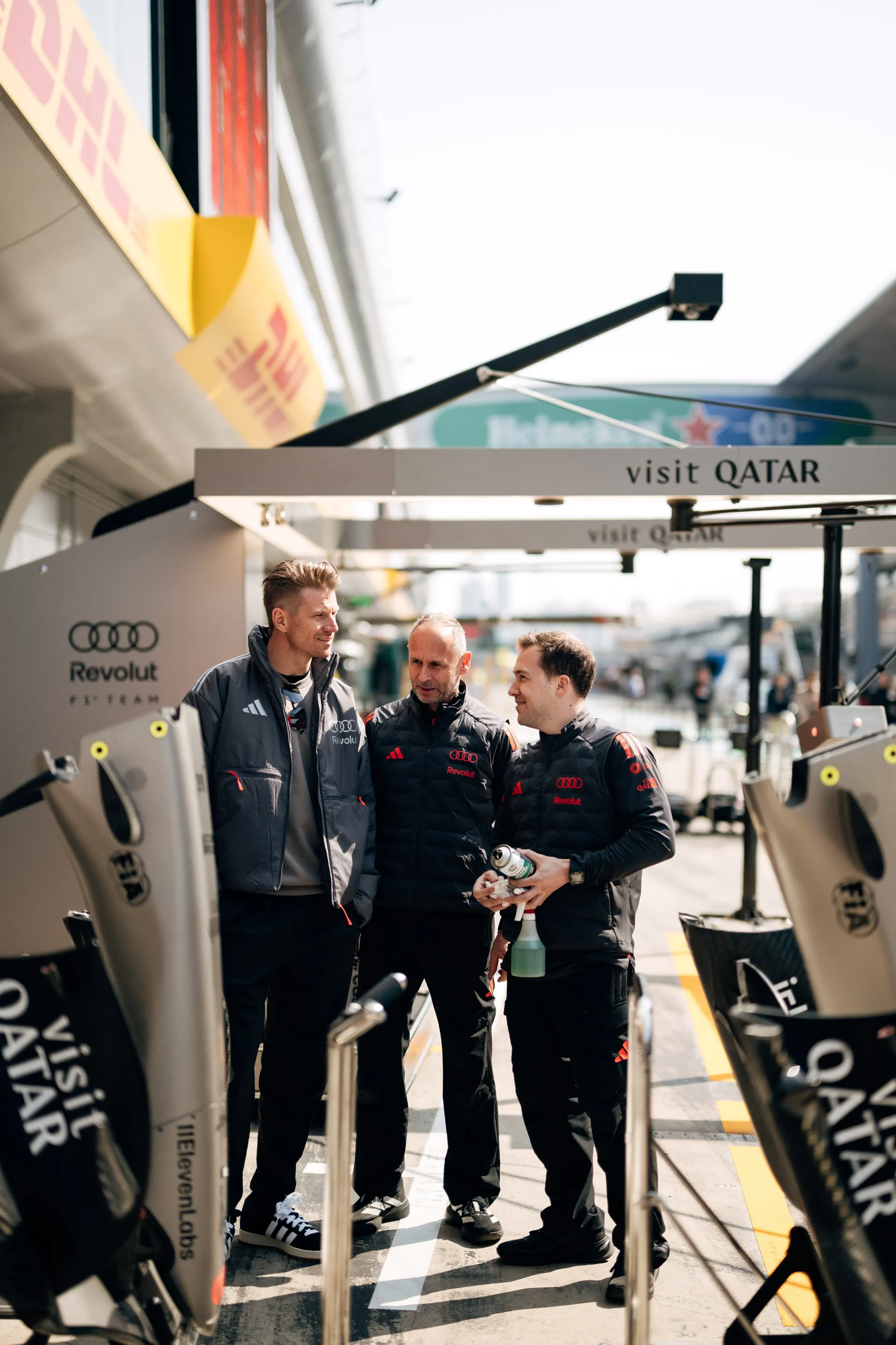 Audi Revolut F1® Team engineers stand between car components in the pit lane at the Chinese Grand Prix.