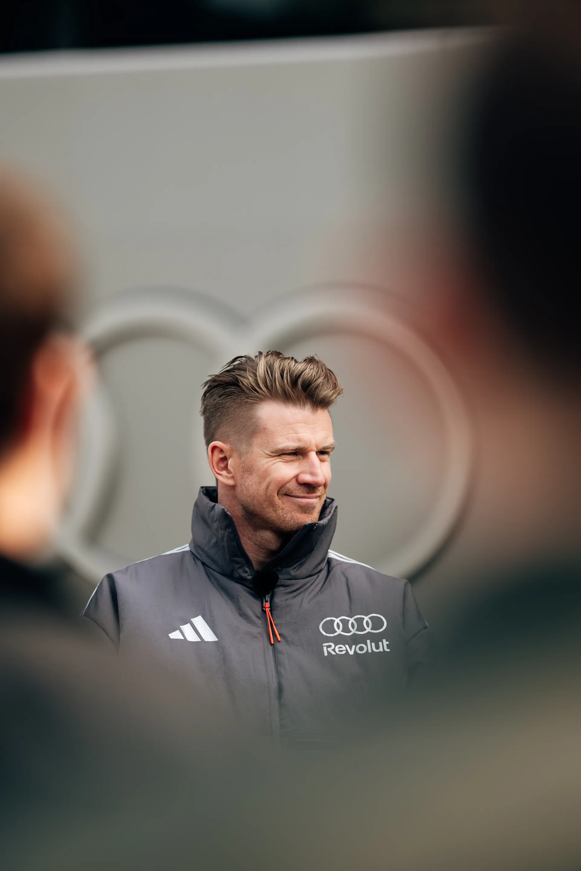 Nico Hulkenberg stands outside the Audi Revolut F1® Team garage in Shanghai, framed by soft foreground blur and Audi rings in the background.