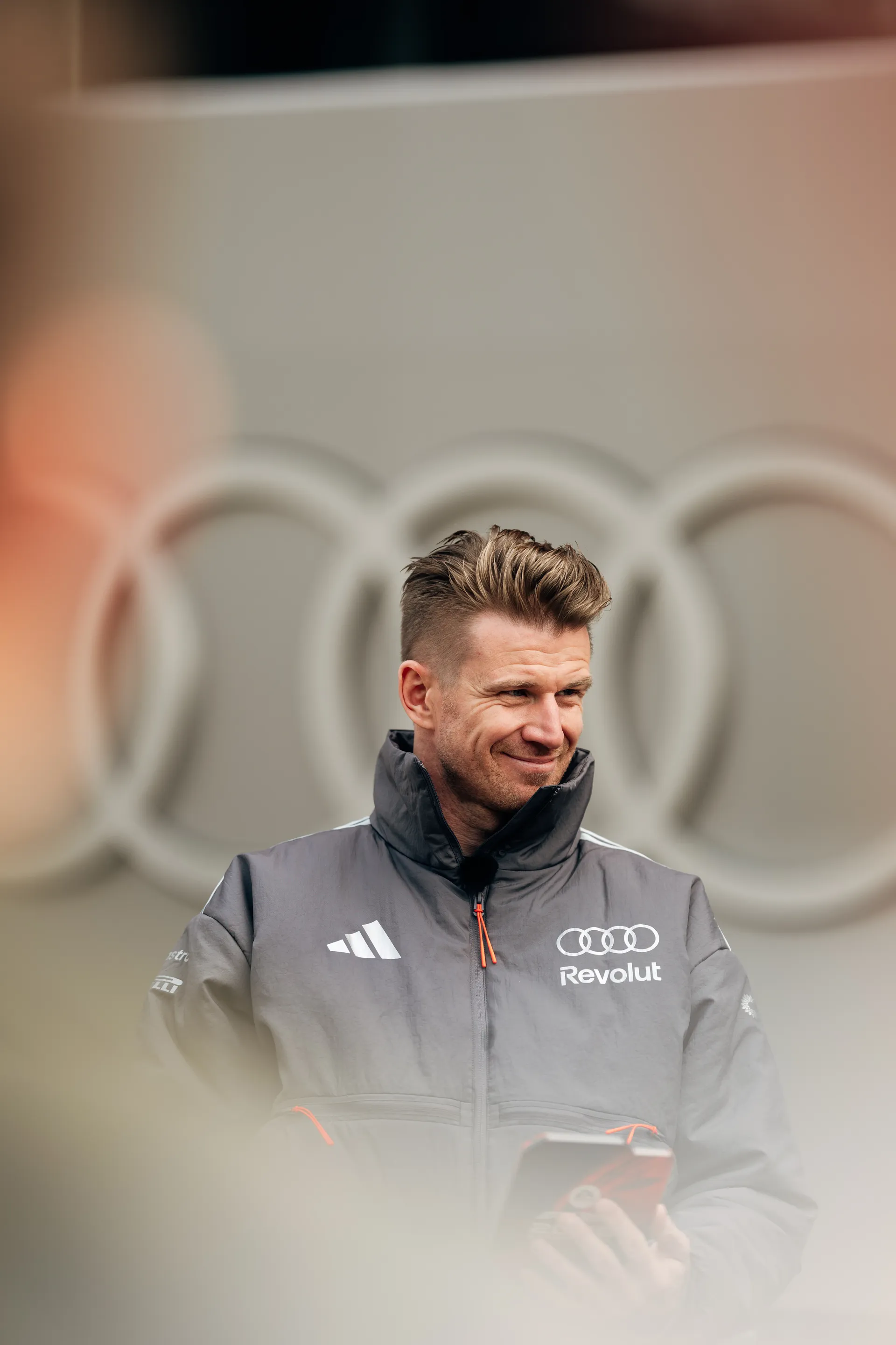 Nico Hulkenberg holds his phone outside the Audi Revolut F1® Team garage, with Audi rings softly visible behind him.