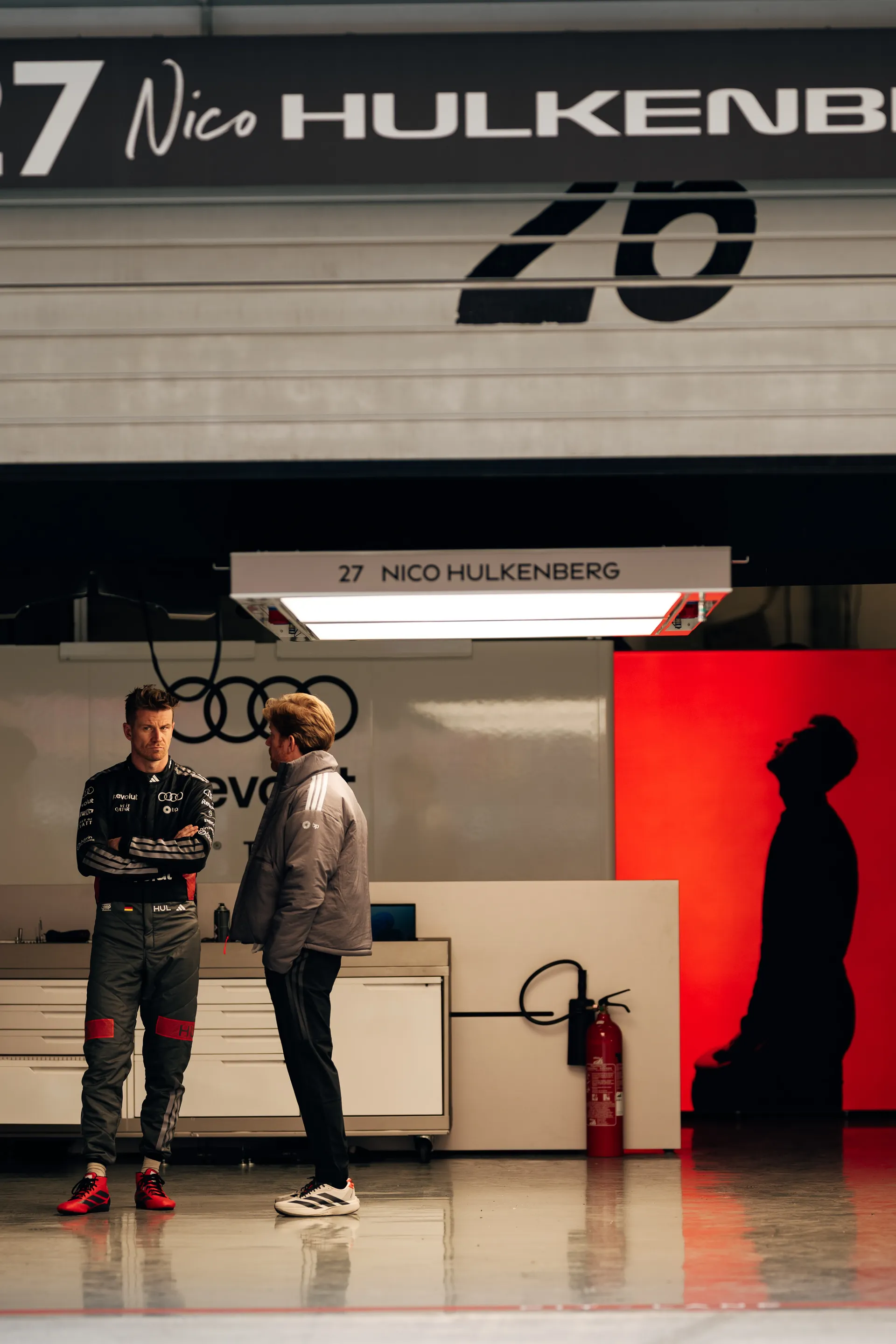 Nico Hulkenberg stands in conversation inside the Audi Revolut F1® Team garage in Shanghai, with dramatic red light and shadows in the background.