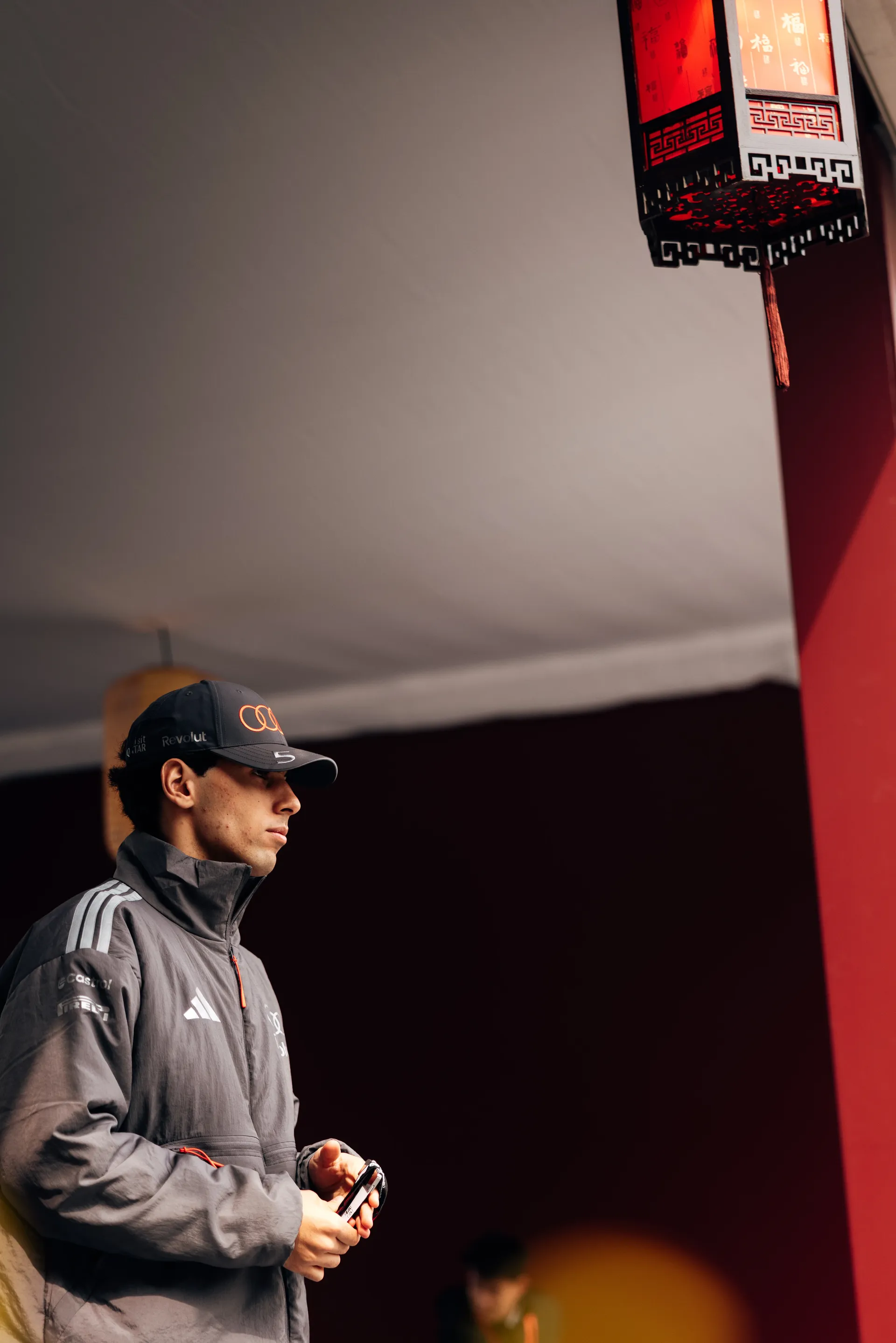 Gabriel Bortoleto stands in Audi Revolut F1® Team outerwear beneath a red lantern during race day arrival at the Chinese Grand Prix.