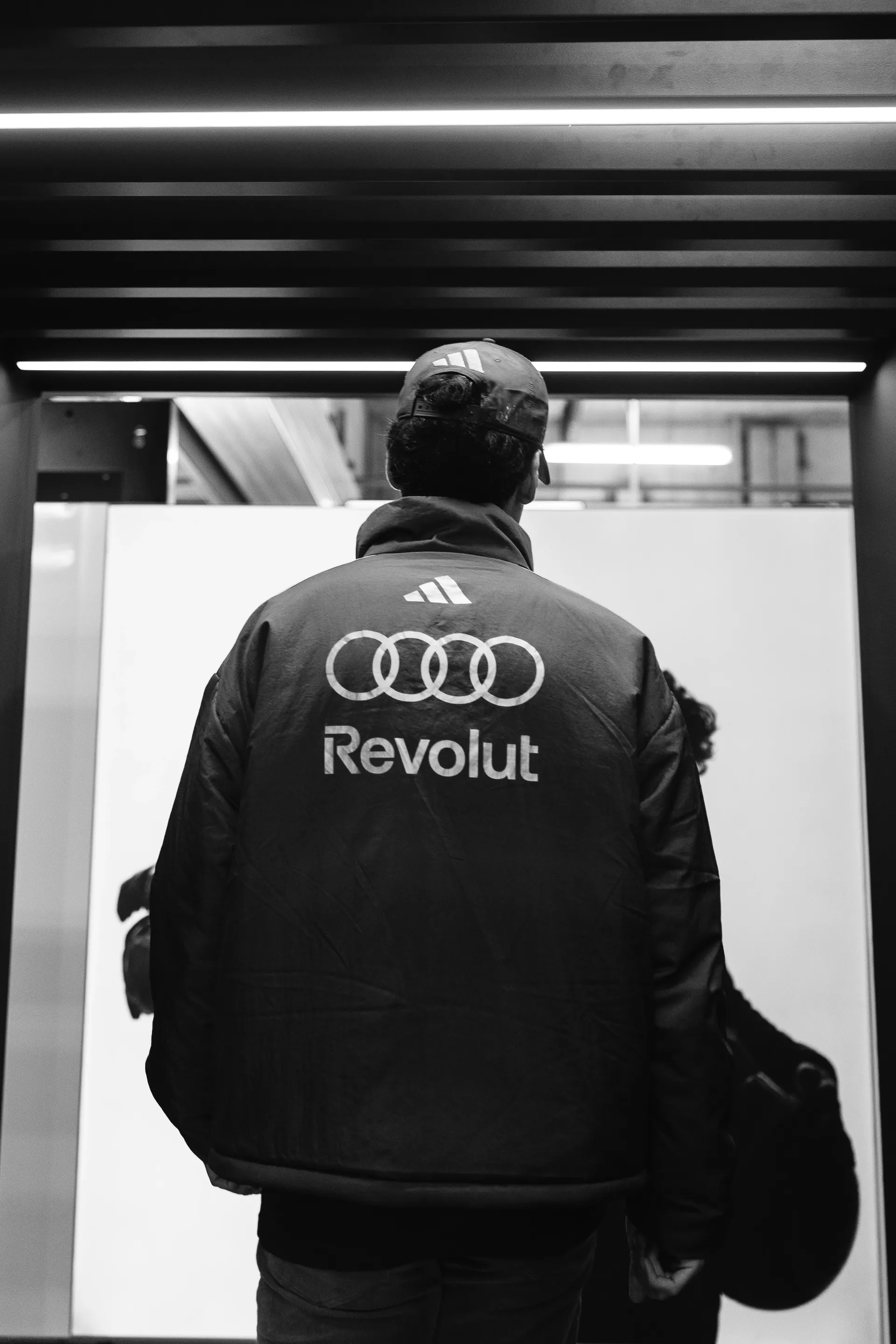 Rear view of Gabriel Bortoleto walking through the garage entrance in Audi Revolut F1® Team outerwear on race day.