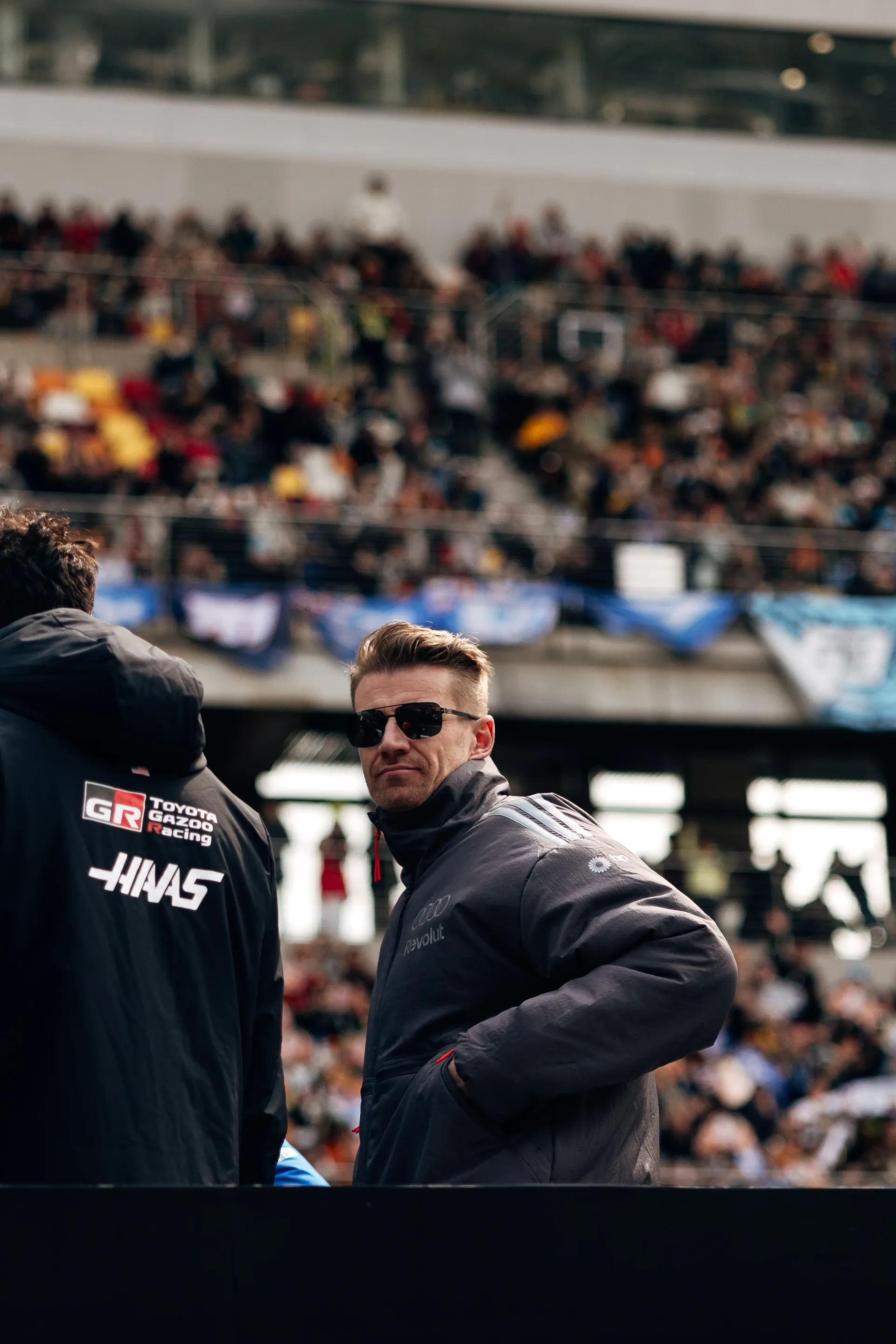 Nico Hulkenberg stands with other drivers during a paddock appearance in front of the crowd at the Chinese Grand Prix, wearing Audi Revolut F1® Team outerwear.