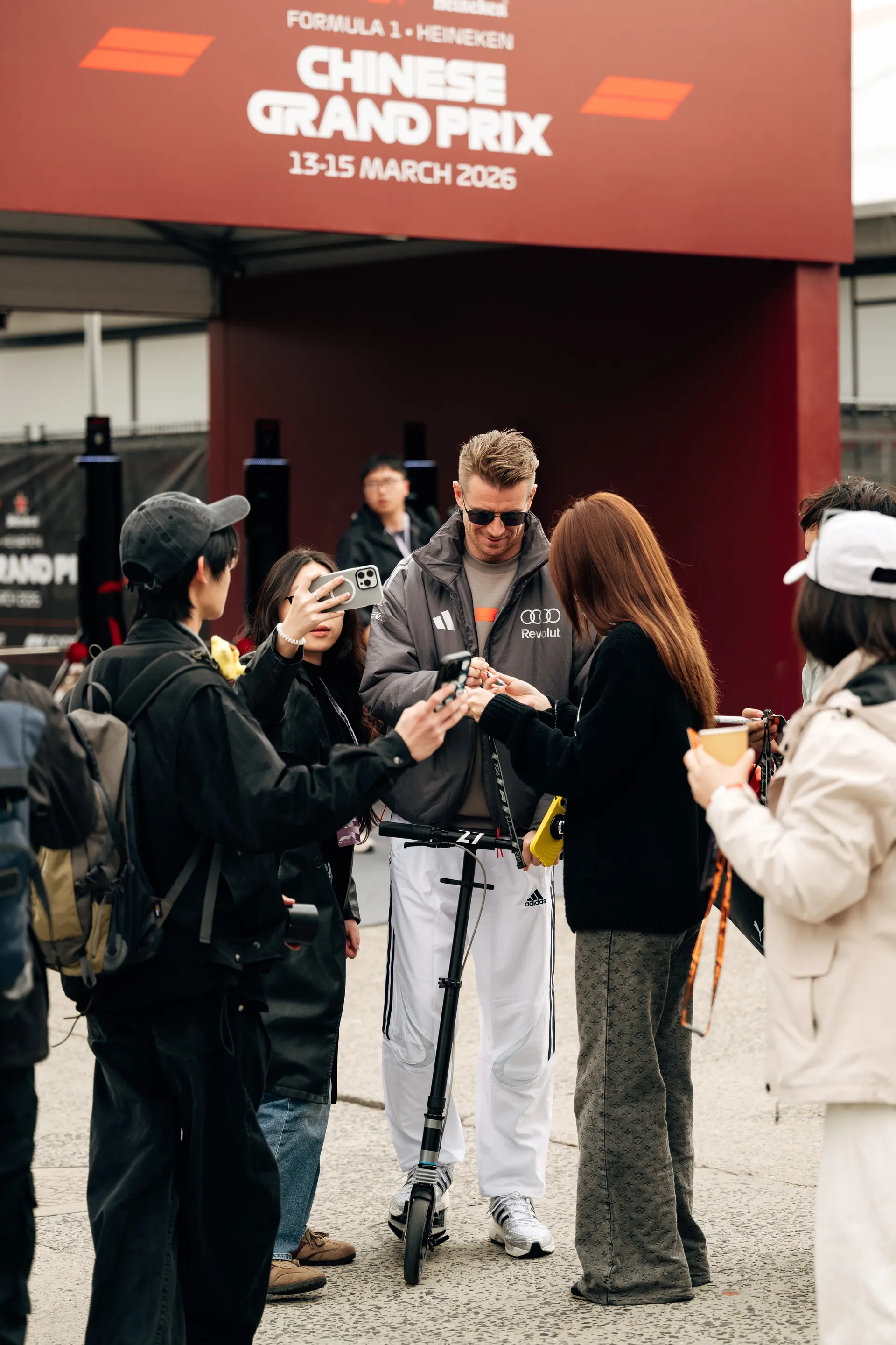 Nico Hulkenberg signs autographs for fans beside his scooter under Chinese Grand Prix signage in the paddock.