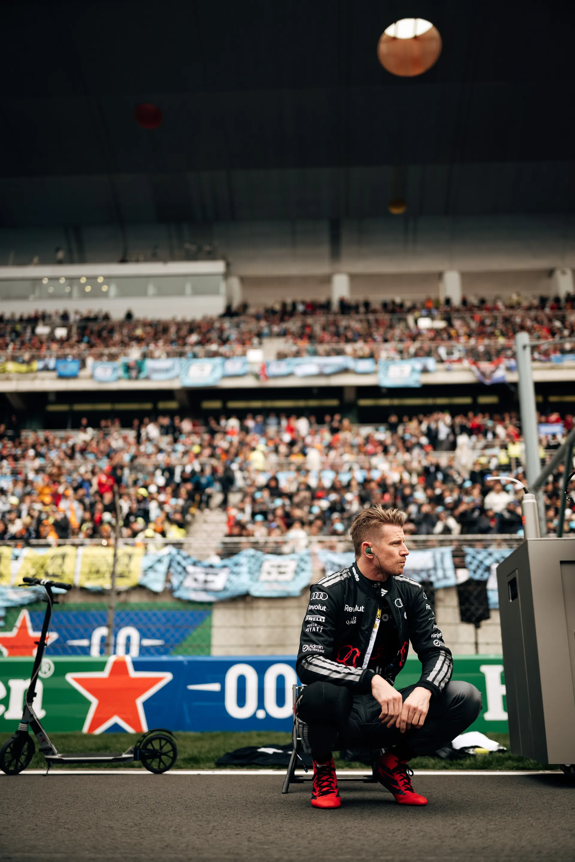 Nico Hulkenberg crouches trackside in full Audi Revolut F1® Team race kit with the Shanghai grandstands in the background.