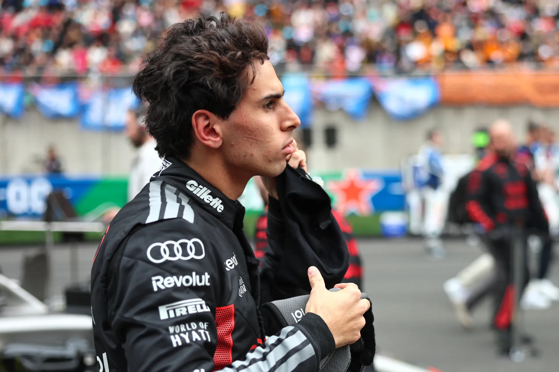 Gabriel Bortoleto stands on the grid in his Audi Revolut F1® Team race suit, holding his balaclava with the Shanghai grandstands in the background.