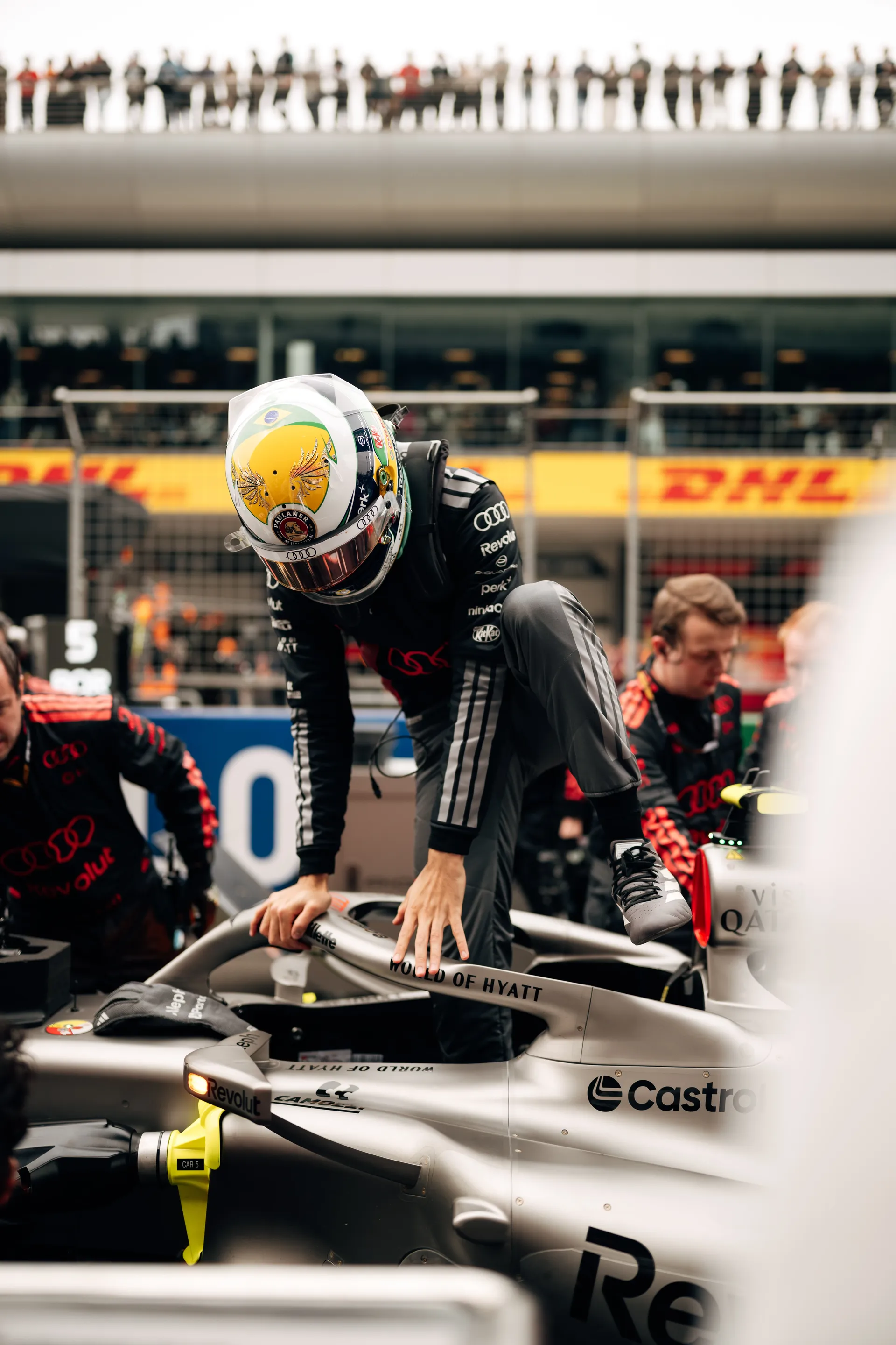Gabriel Bortoleto climbs out of the Audi Revolut F1® Team car on the grid before the Chinese Grand Prix, wearing his green and yellow helmet.