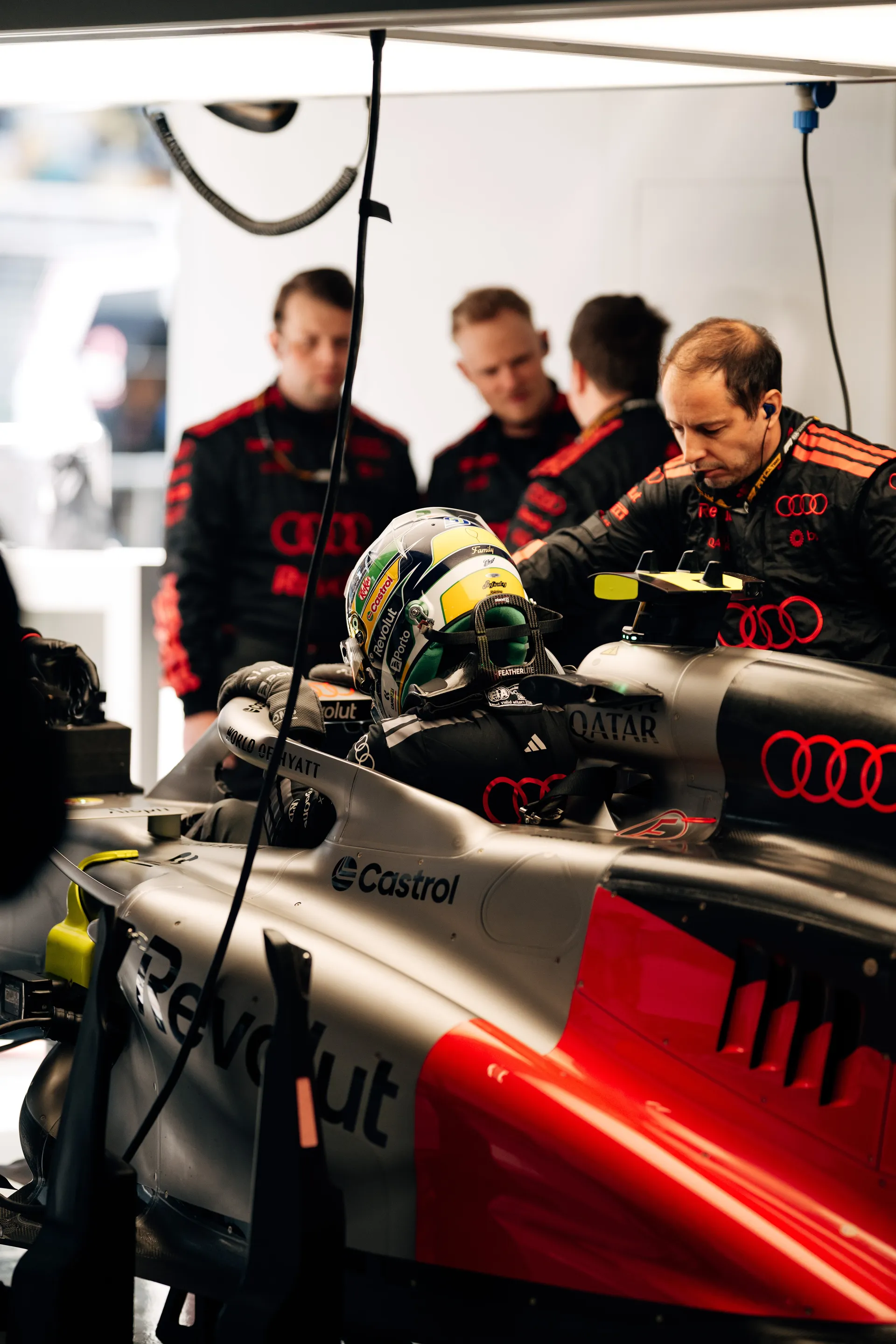An Audi Revolut F1® Team driver sits in the car inside the garage while mechanics work around the cockpit during the Chinese Grand Prix weekend.