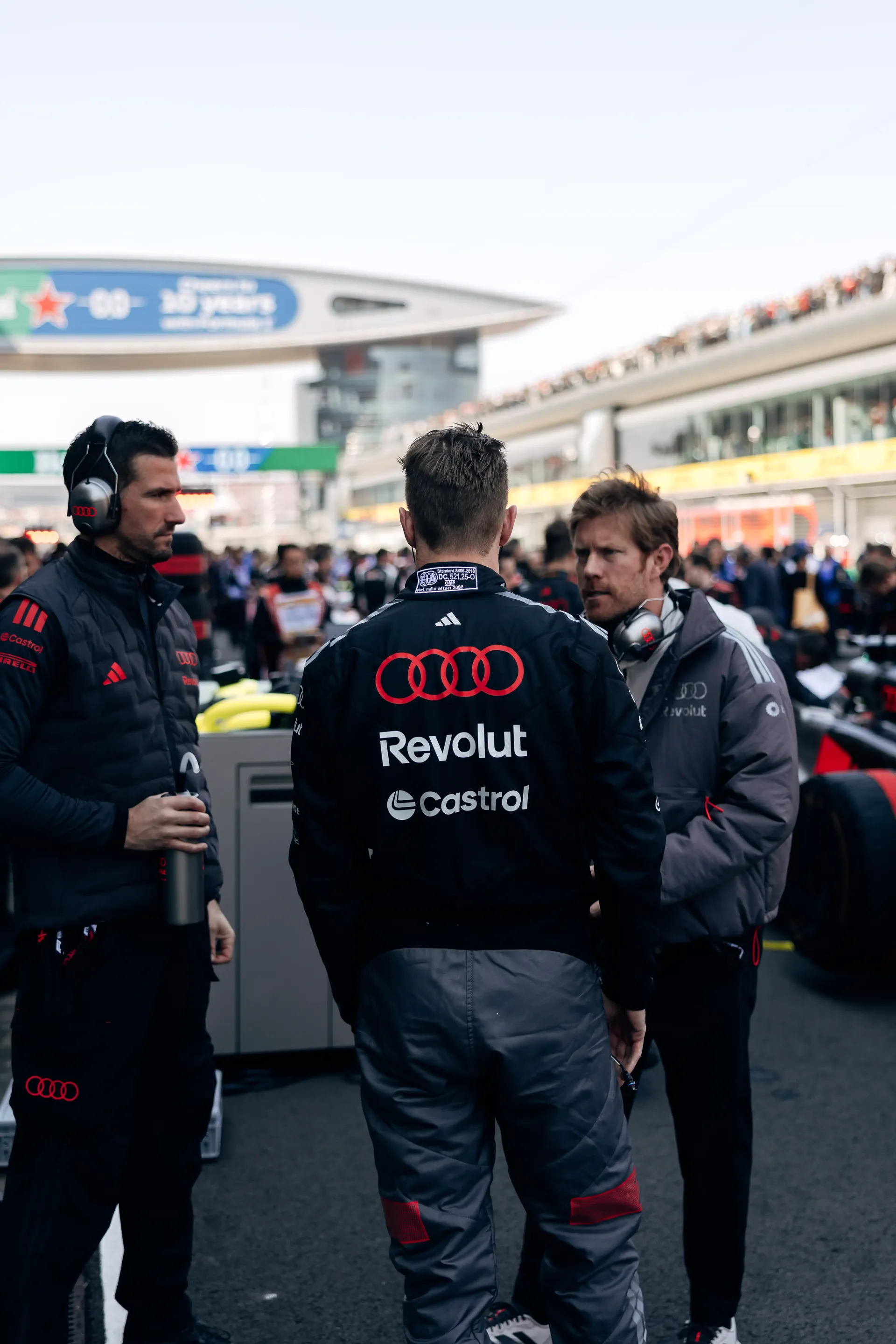 Audi Revolut F1® Team drivers and team members gathered beside the Formula 1 car in the pit lane.