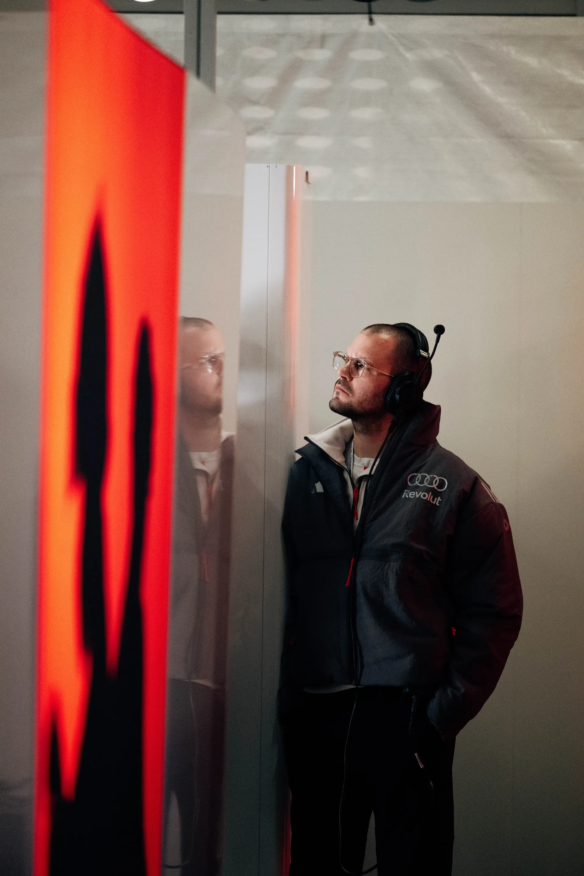 Audi Revolut F1® Team staff member standing beside illuminated Audi branding in the paddock area.