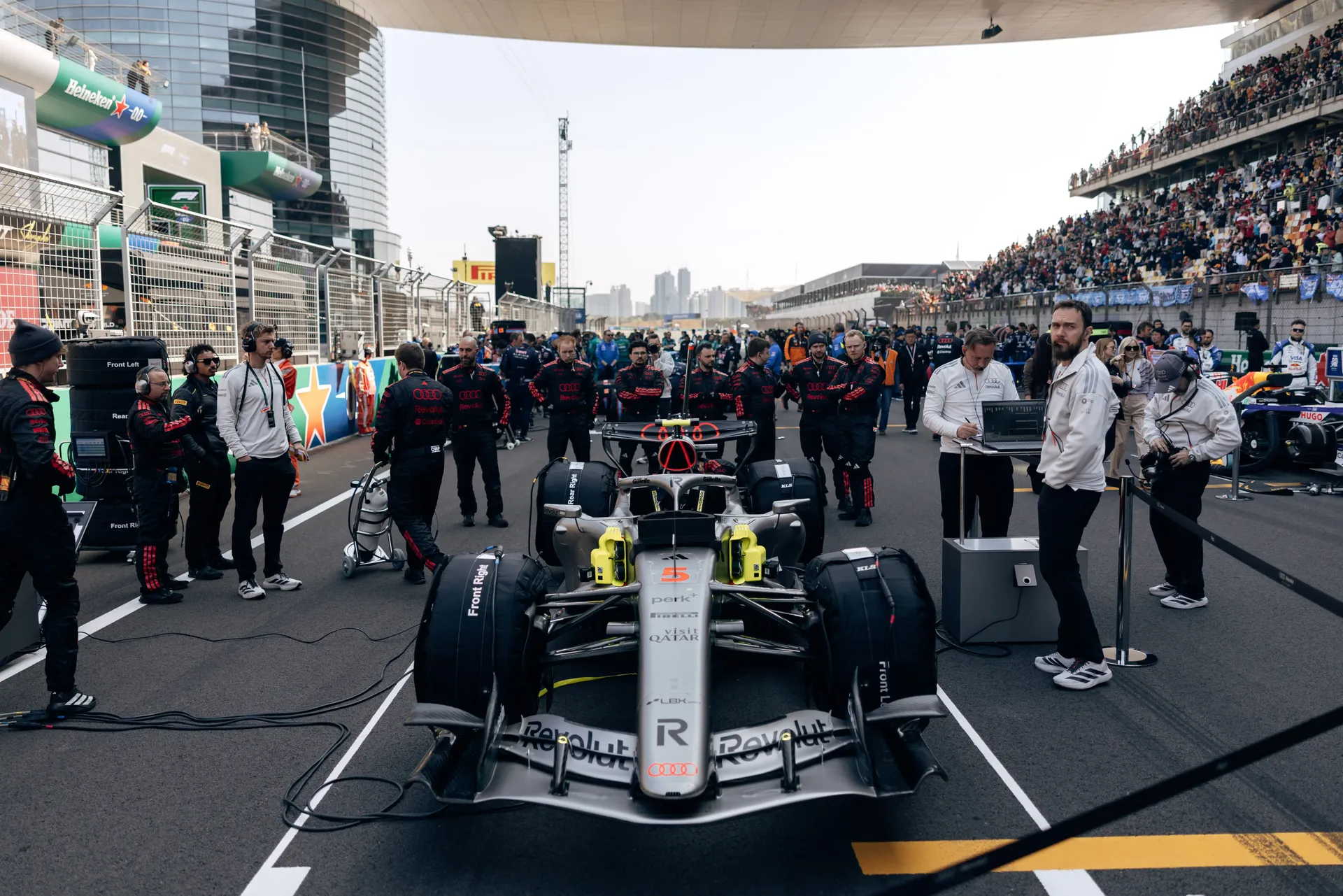 Audi Revolut F1® Team crew standing in formation on the starting grid at the Chinese Grand Prix sprint event with the car ahead and grandstands full.