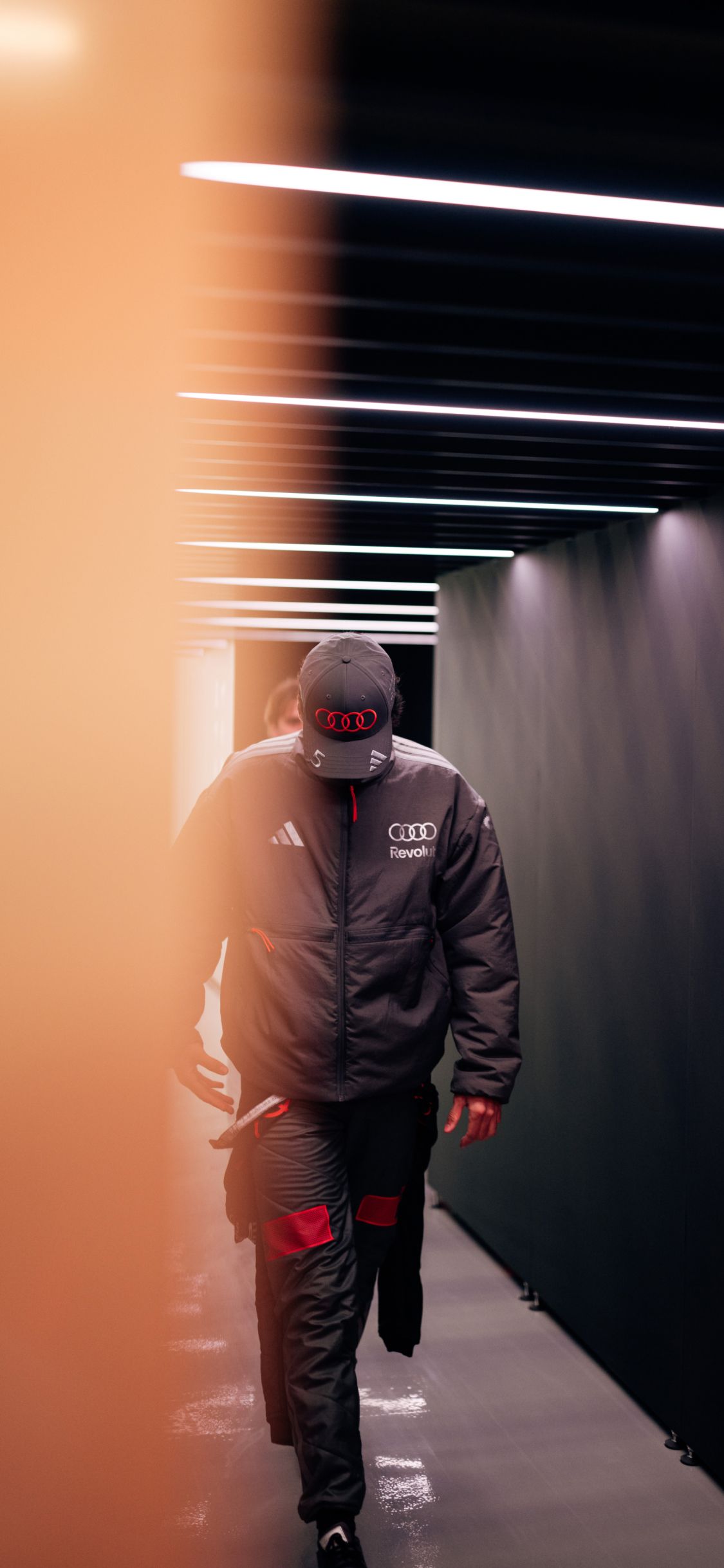 Gabriel Bortoleto walks through a lit corridor in Audi Revolut F1® Team outerwear before the Chinese Grand Prix.