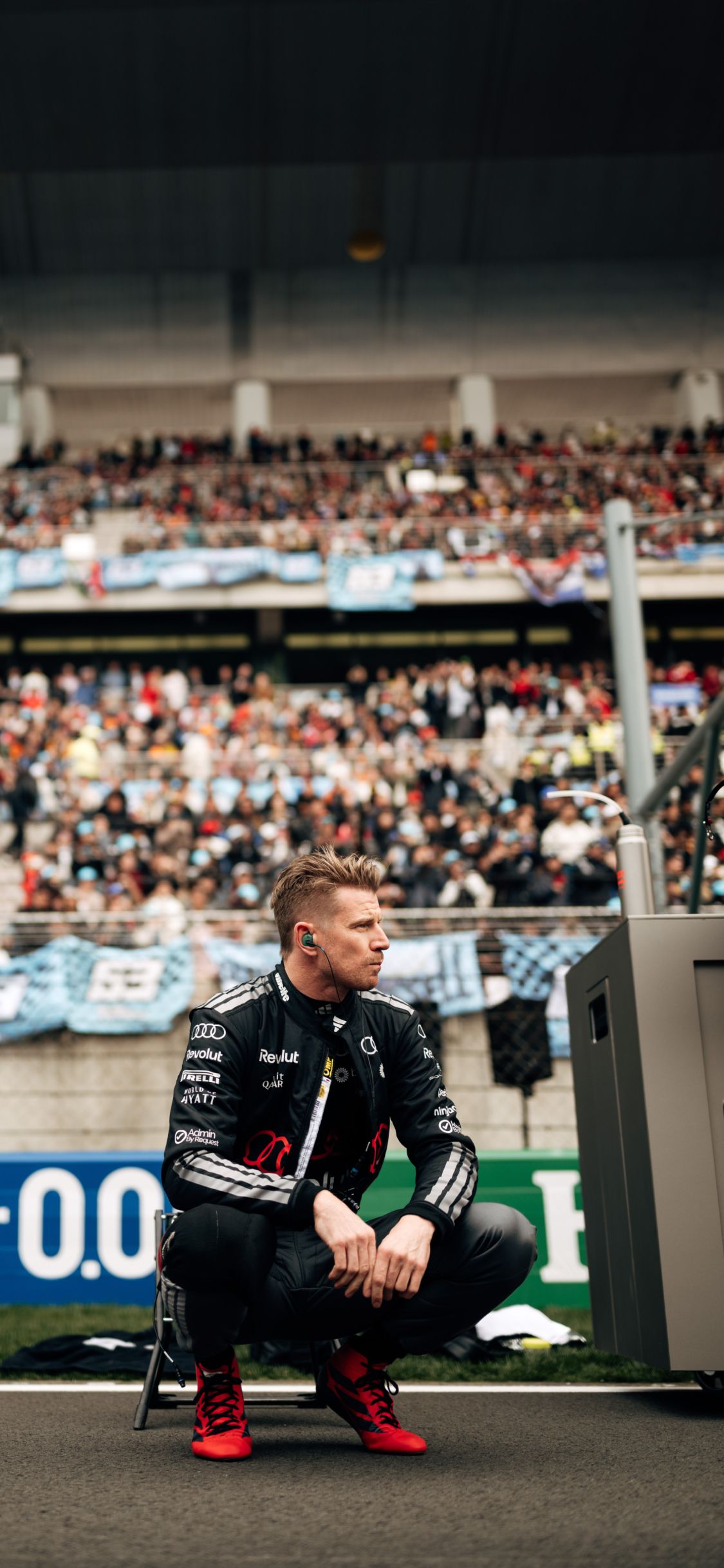 Nico Hulkenberg crouches trackside in full Audi Revolut F1® Team race kit with the grandstands in the background in Shanghai.
