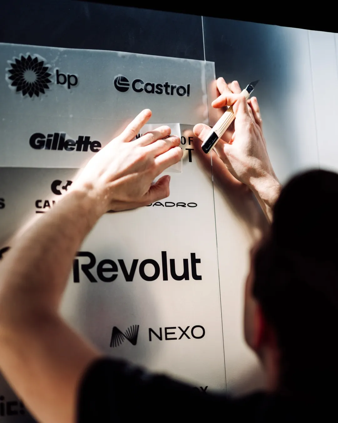 Close up of hands applying partner decals on a garage wall during Bahrain Testweek 2026 from Audi Revolut F1® Team