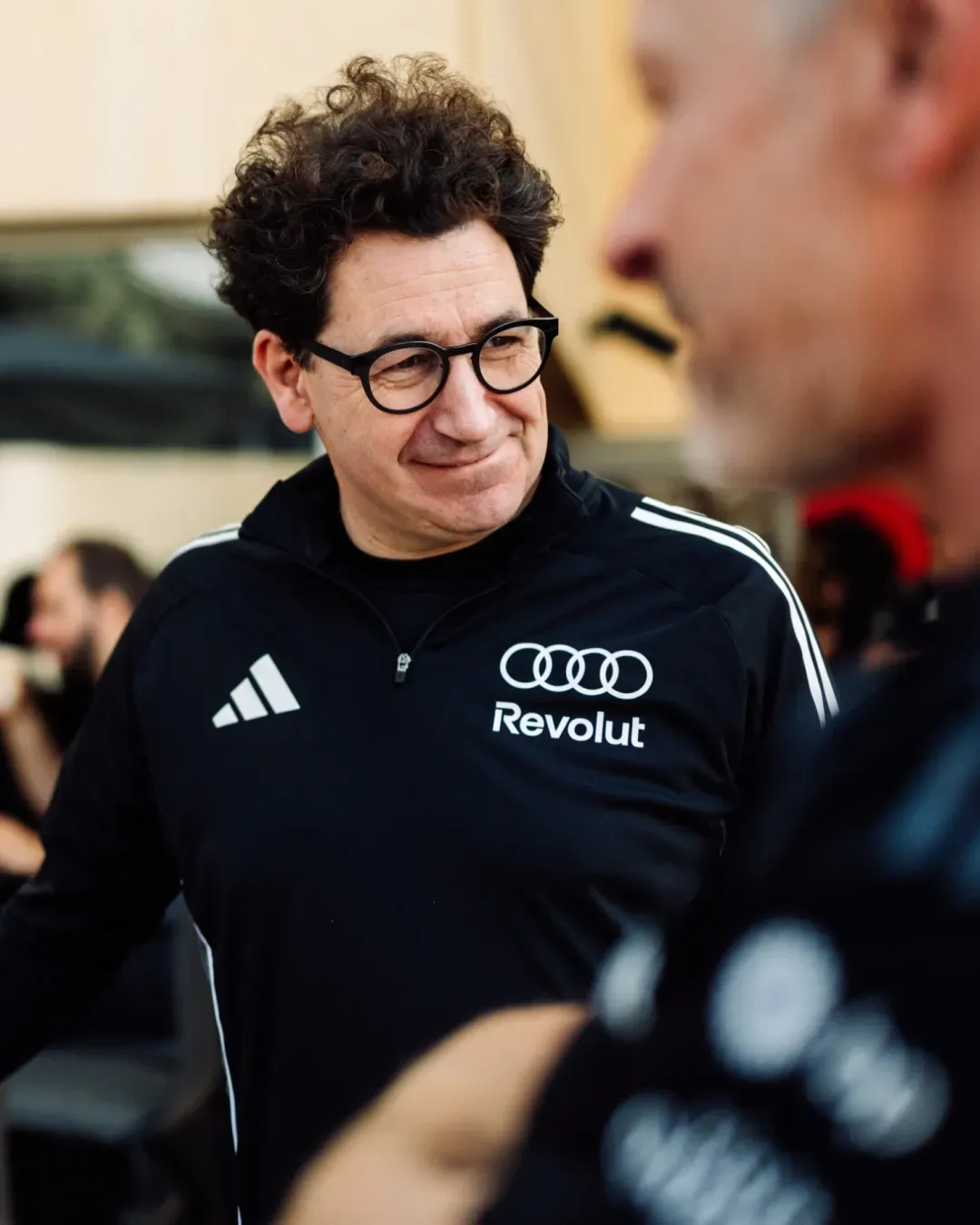 Audi Revolut F1® Team leader in black adidas jacket listens during a paddock conversation, shallow depth of field.