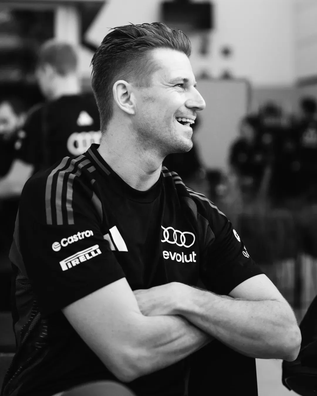 Black and white portrait of an Audi Revolut F1® Team member smiling with arms crossed in the garage.
