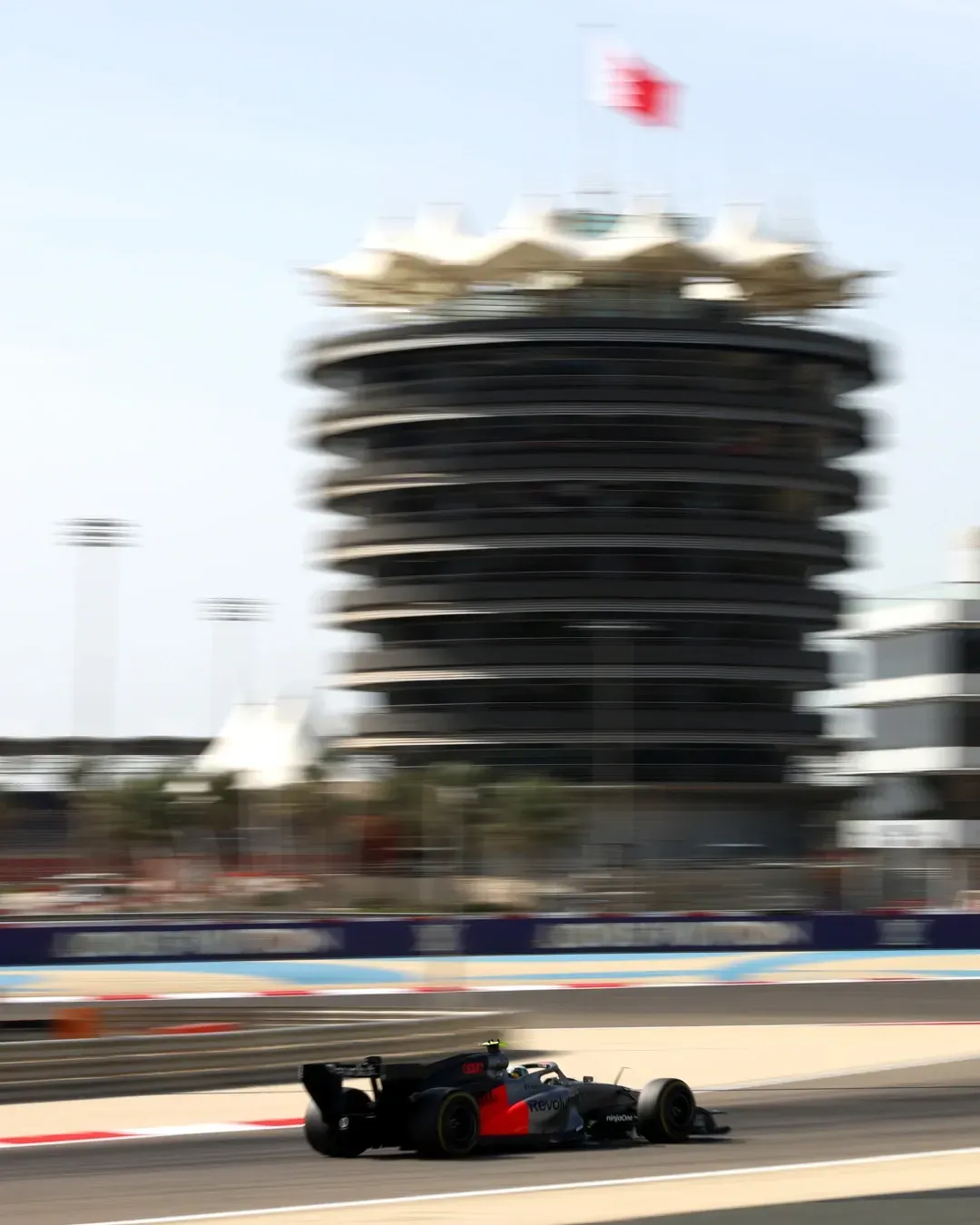 Panning shot with Bahrain tower blurred behind as the Audi Revolut F1® Team car streaks along the circuit.