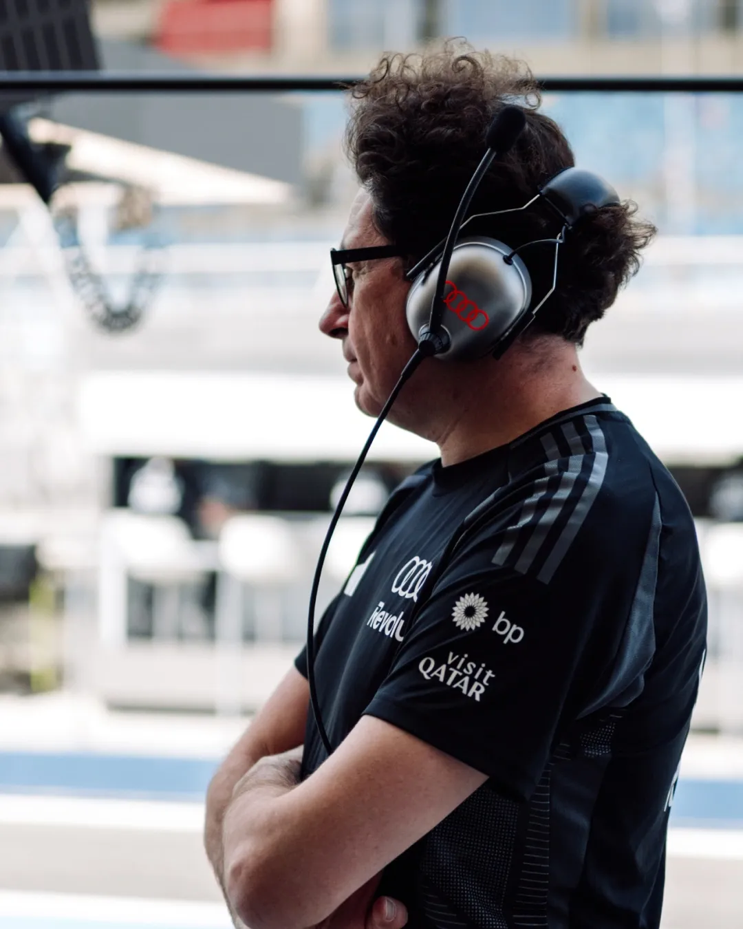 Audi Revolut F1® Team engineer wearing a headset watches the pit lane in profile, arms crossed.
