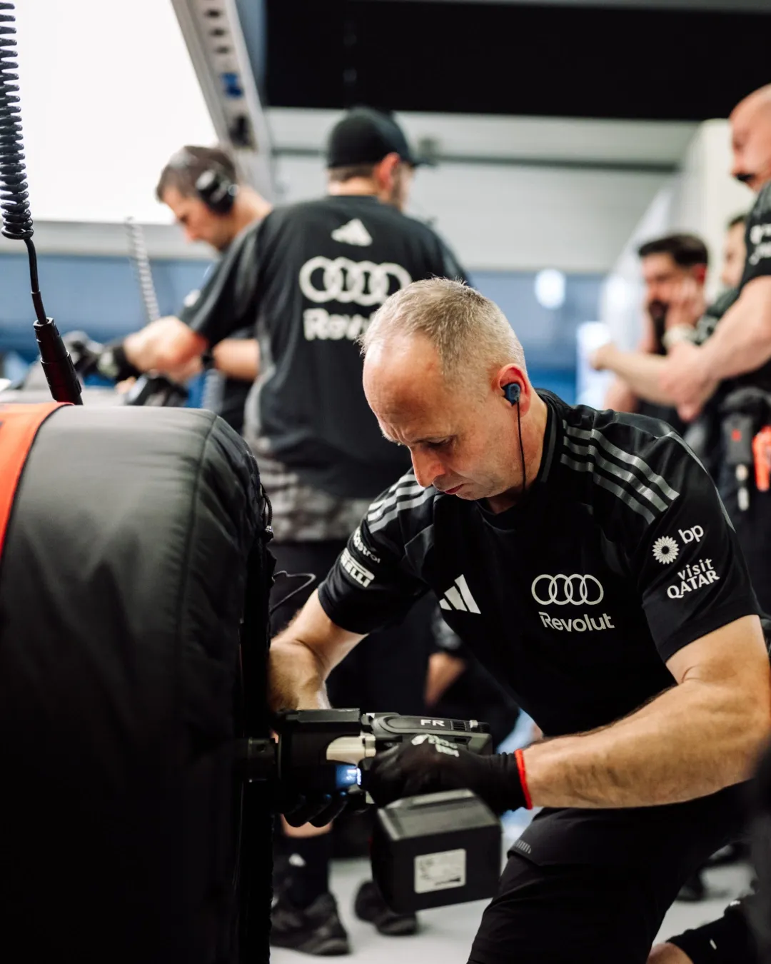 Mechanic uses a wheel gun on a tyre as the team works in the garage.