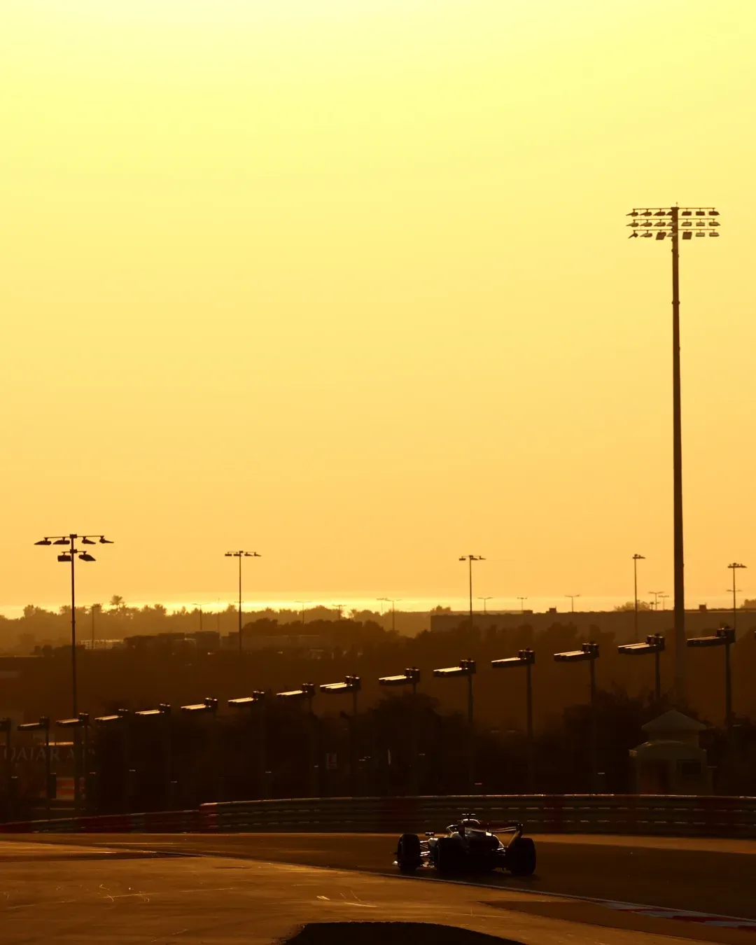 Wide sunset shot of the circuit with the car small on the racing line.