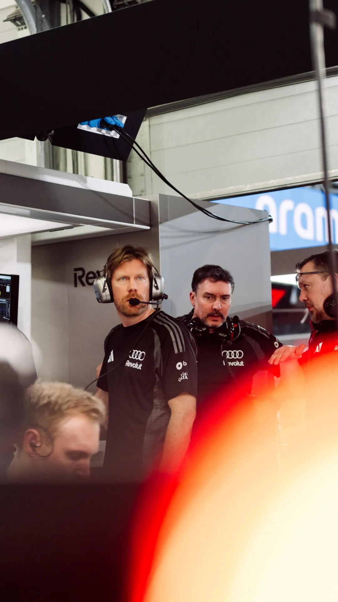 Engineers in the garage wear headsets while monitoring the car and data screens.