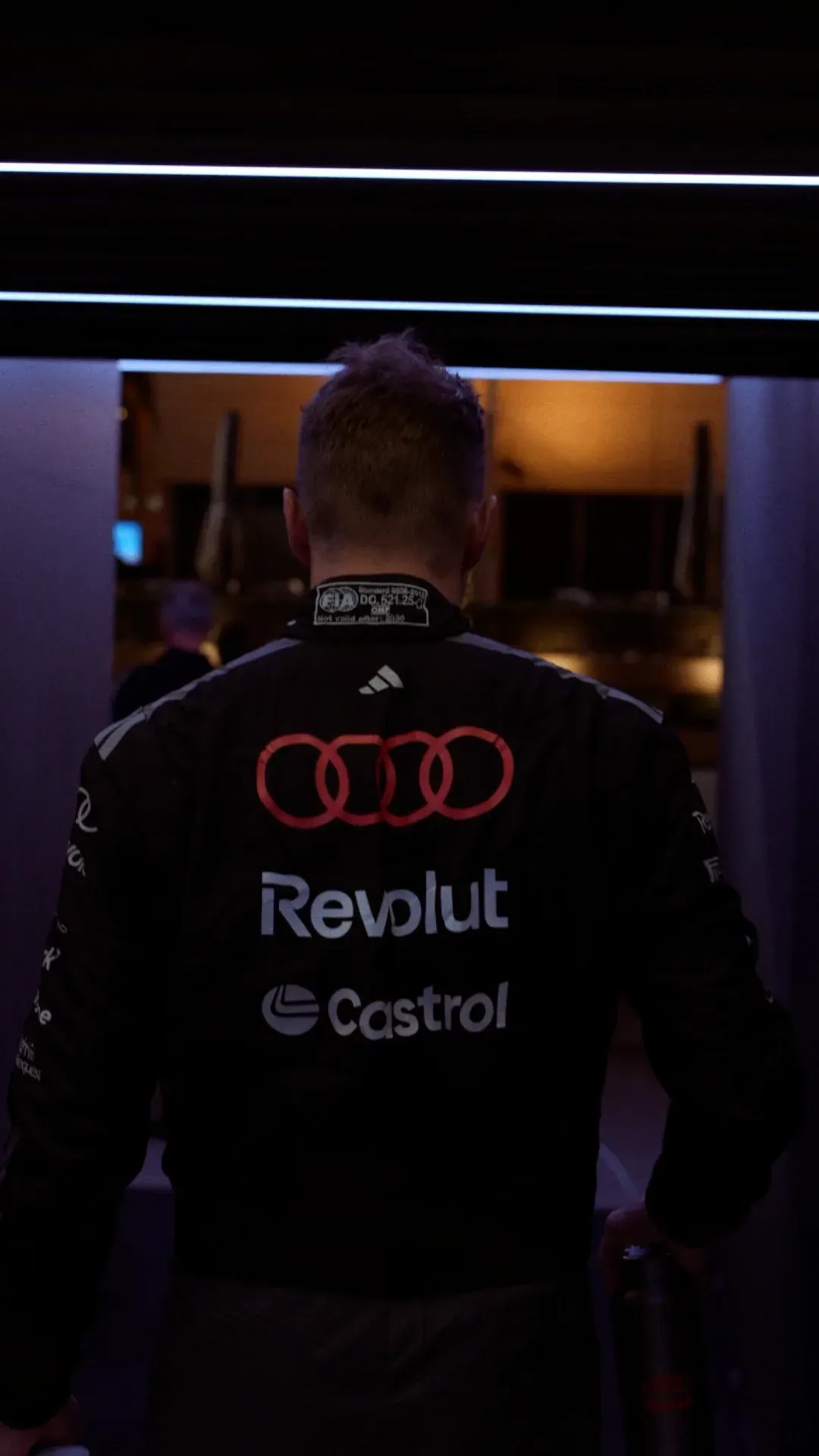 Back view of a team member Nico Hulkenberg walking into a tunnel wearing Audi, Revolut and Castrol branding.