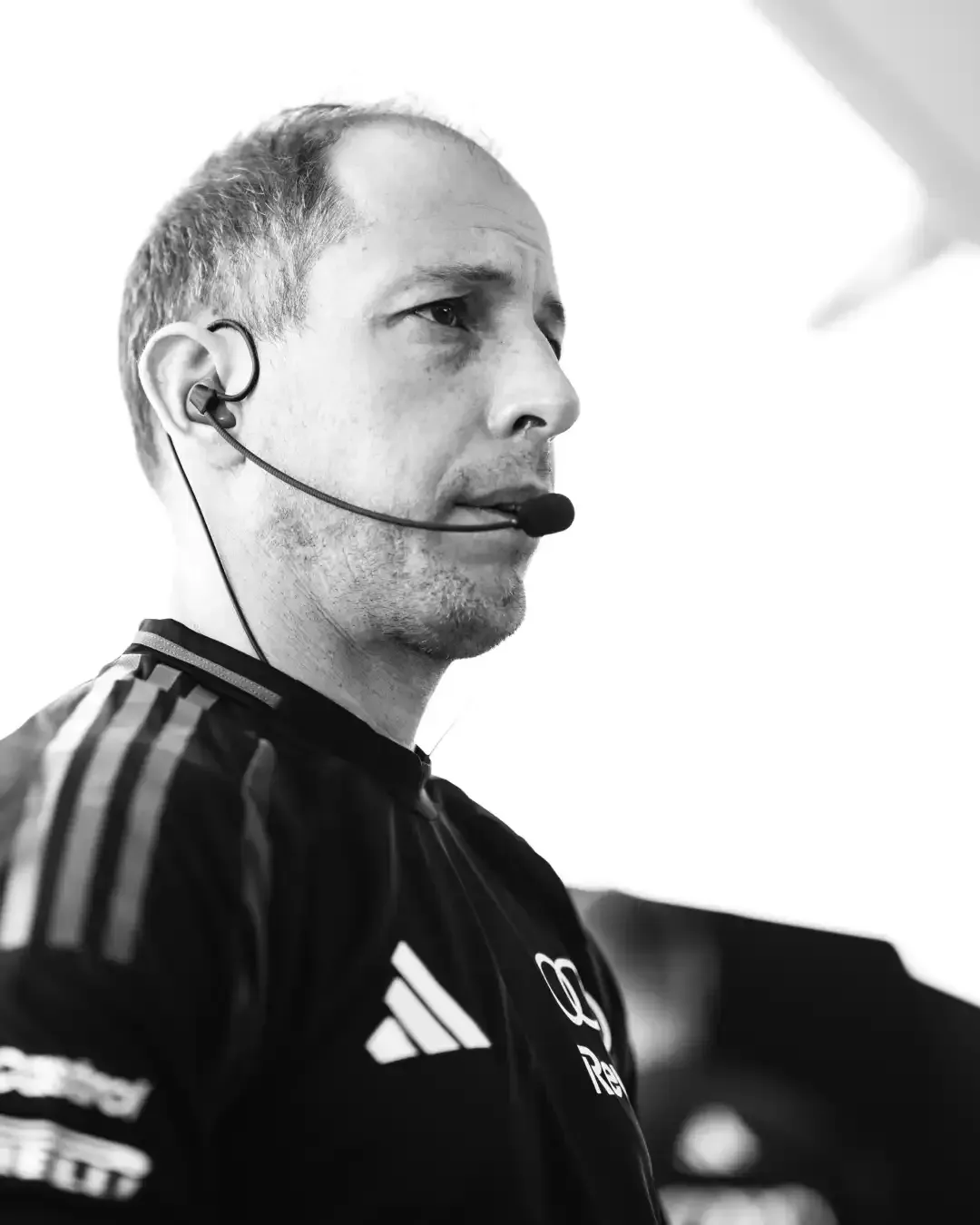 Black and white portrait of an Audi Revolut F1® Team crew member wearing a headset microphone in the garage.