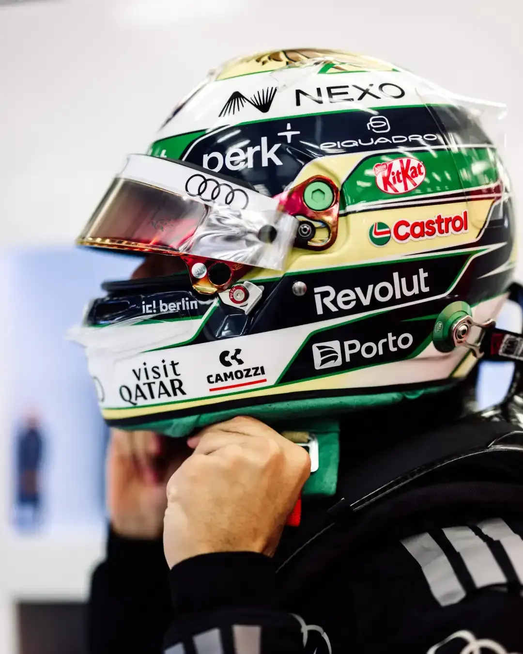 Side view close up of a driver helmet with Audi rings and sponsor logos as a hand adjusts the chin strap.