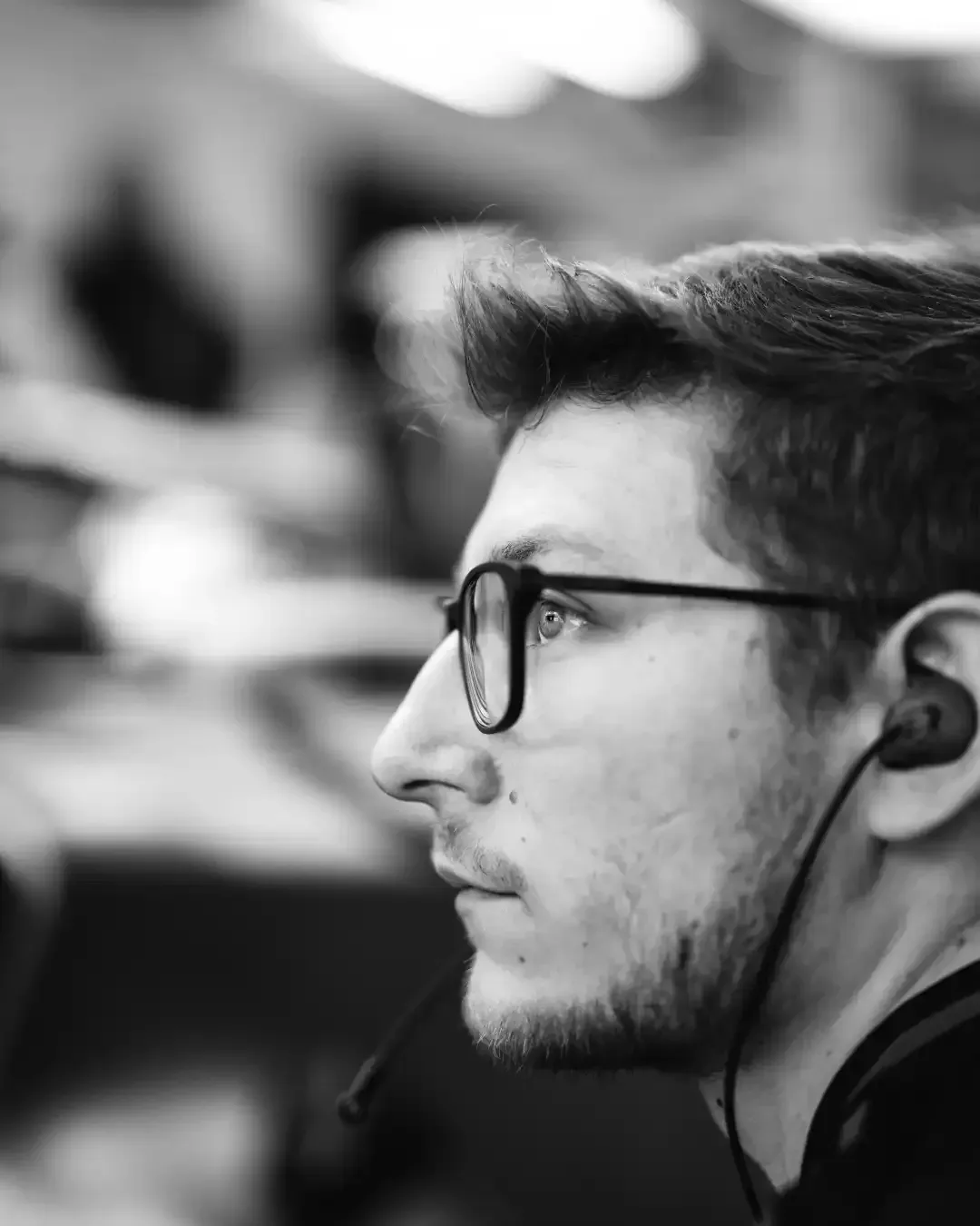 Black and white profile of a team engineer with glasses and in ear comms, focused in the garage.