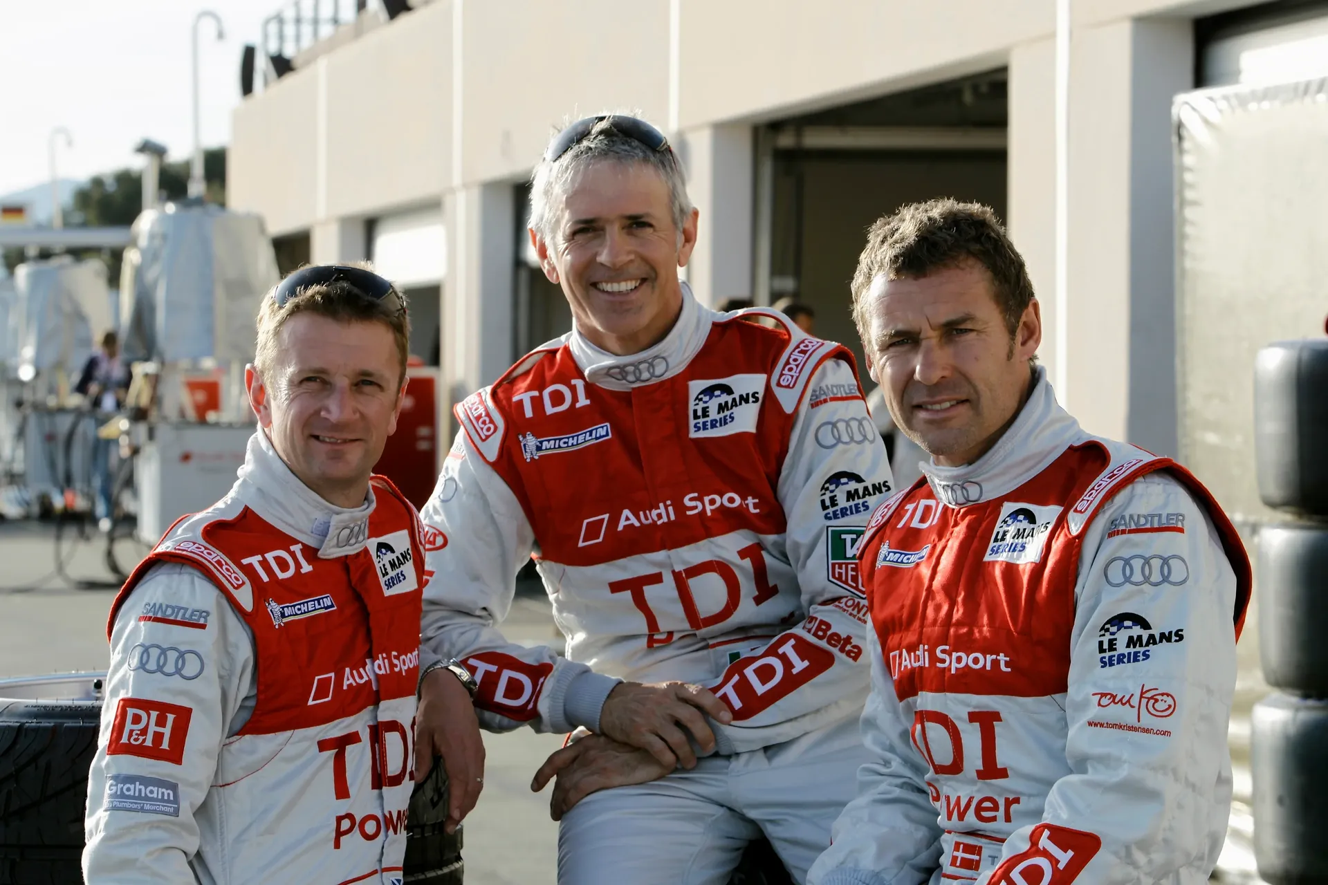 Tom Kristensen and Allan McNish pose together in Audi Sport race suits during their endurance racing career.