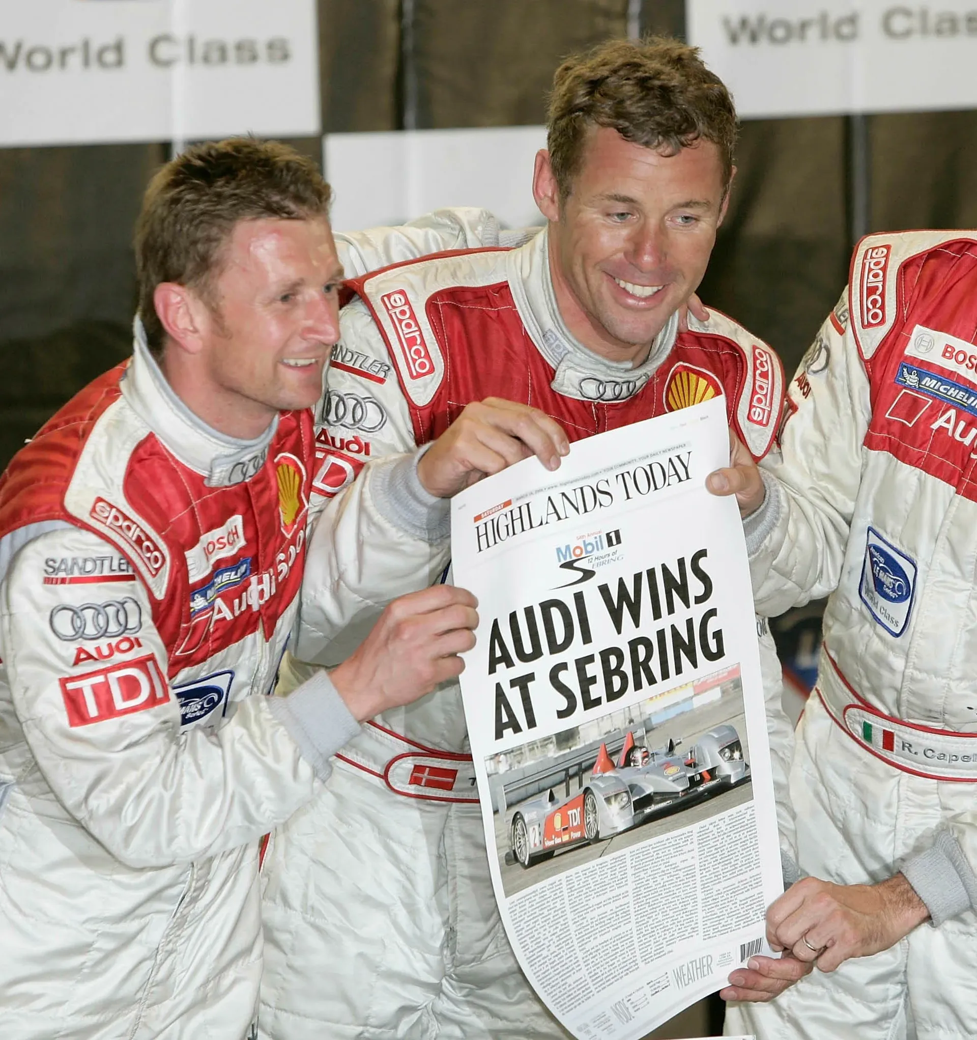 Tom Kristensen and Allan McNish celebrate an Audi Sport victory while holding a newspaper after the Sebring 12 Hours.