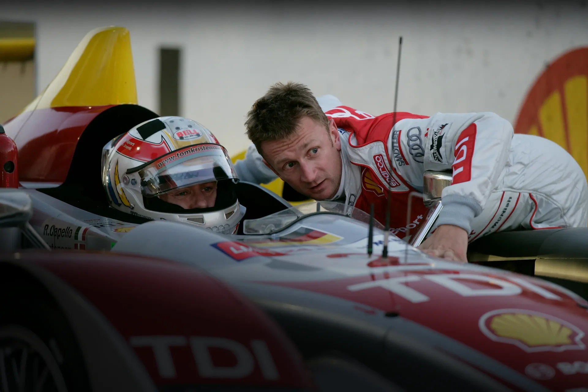 Allan McNish leans over an Audi Sport prototype while Tom Kristensen sits in the cockpit during testing.