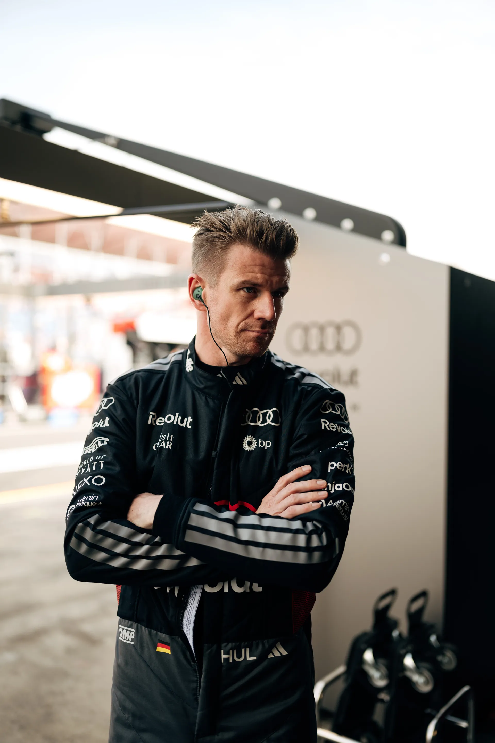 An Audi Revolut F1® Team driver Nico Hulkeberg waits at the garage entrance in race suit and earpiece before a qualifying session.