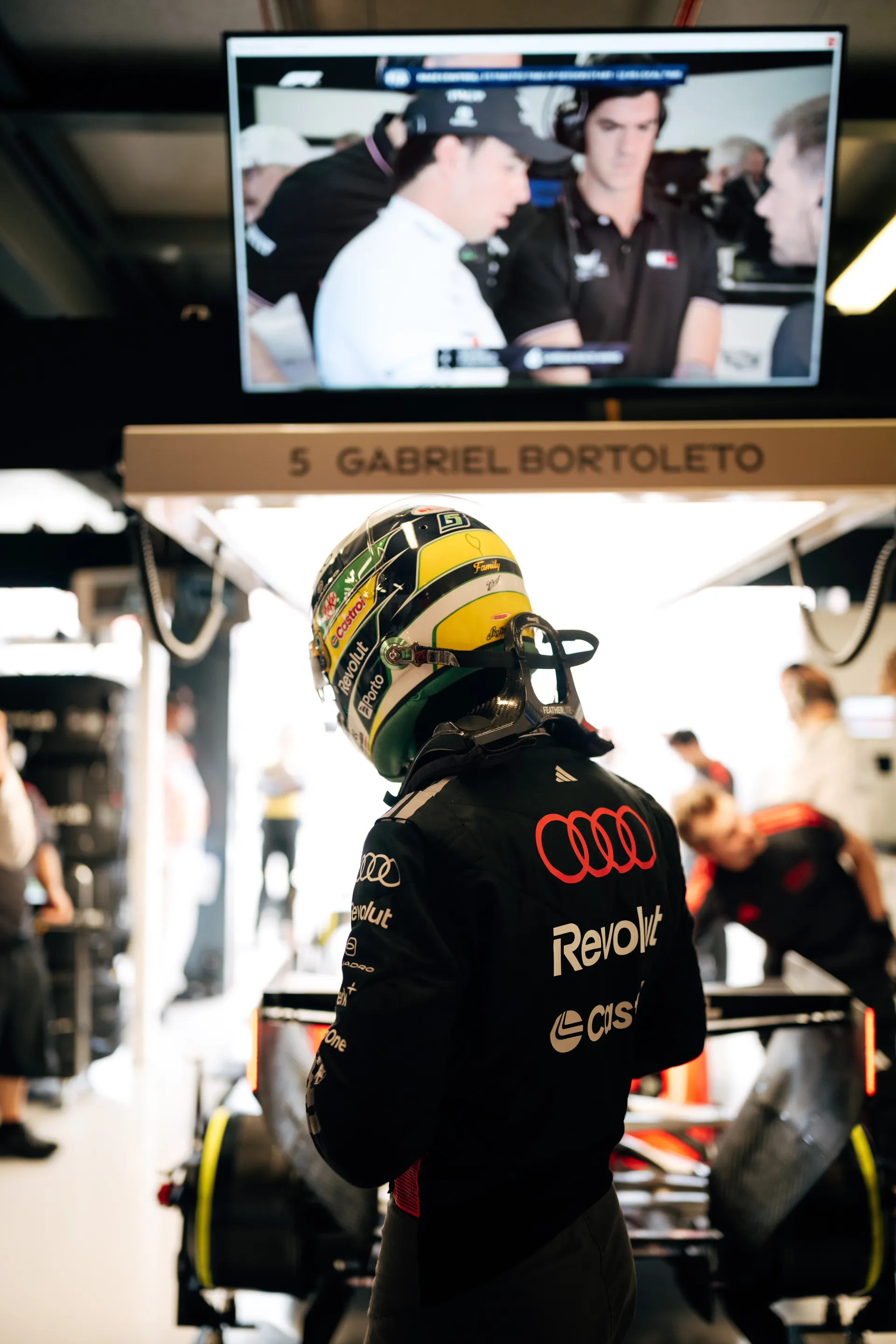 An Audi Revolut F1® Team driver Gabriel Bortoleto stands in front of the garage and car setup beneath a Gabriel Bortoleto name board.