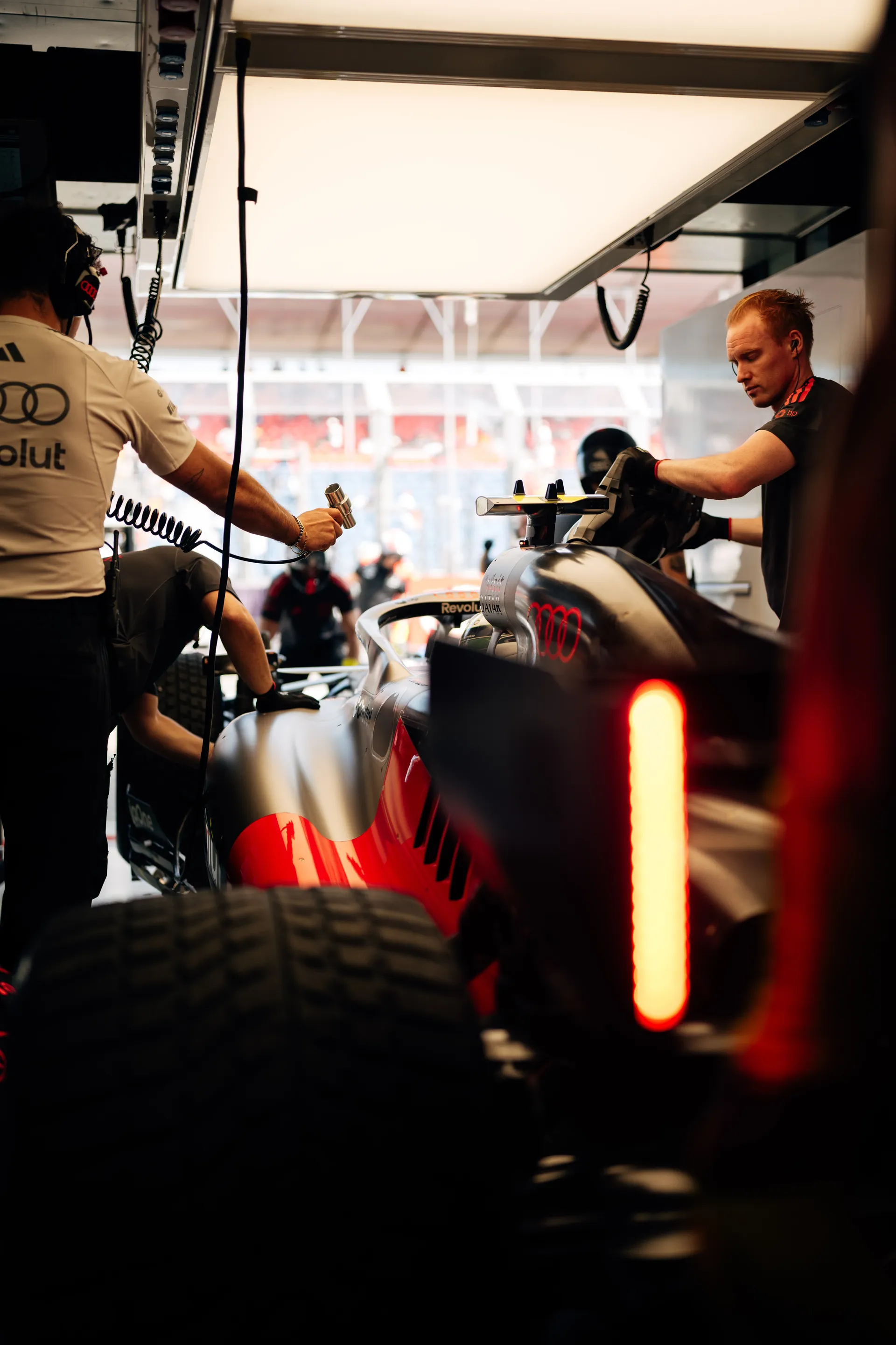 Audi Revolut F1® Team mechanics work on the car inside the garage under bright overhead lights before qualifying.