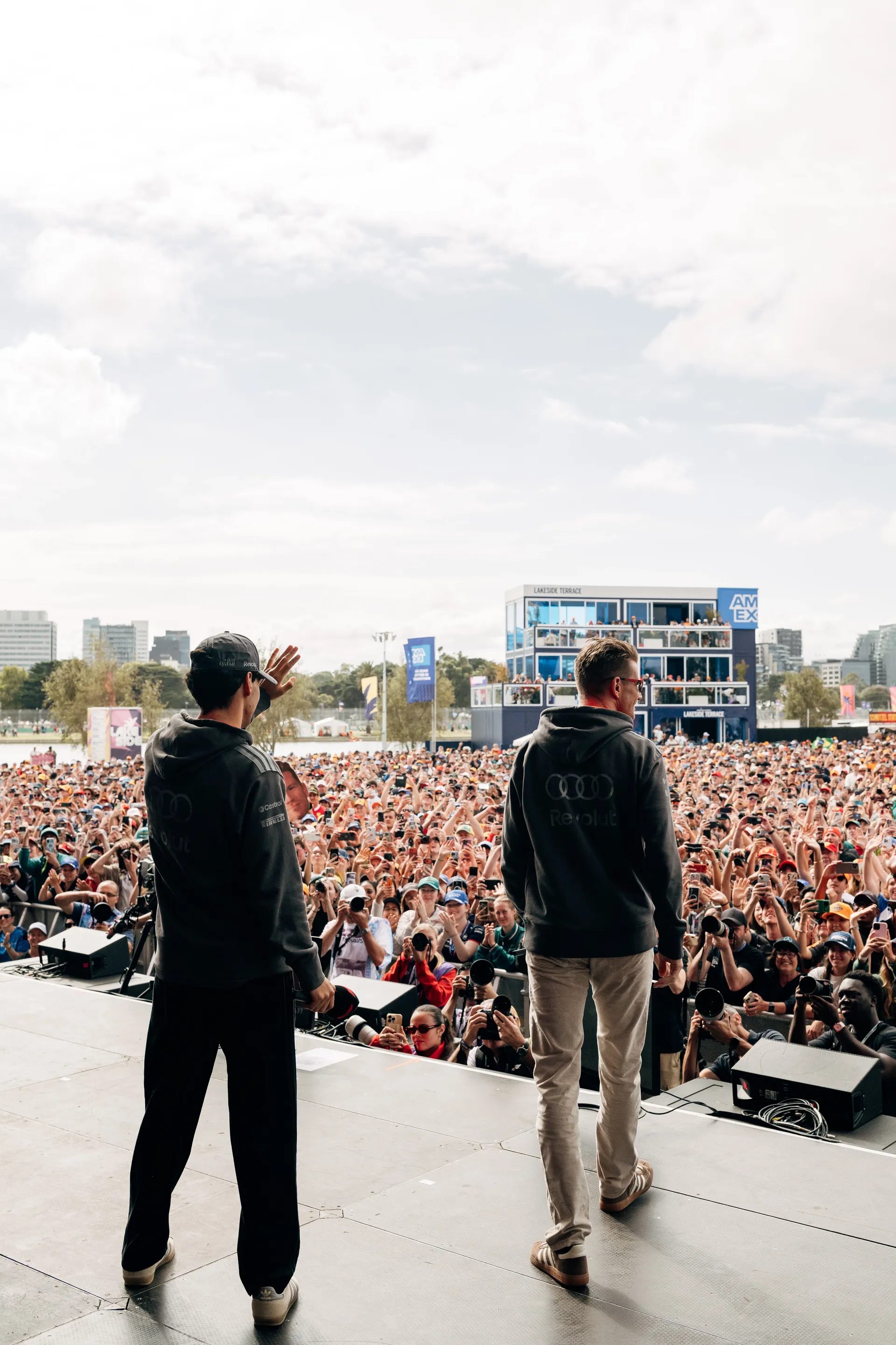 Two Audi Revolut F1® Team drivers Niko Hulkenberg and Gabriel Bortoleto wave to a packed crowd from the stage during a live fan event in Melbourne.