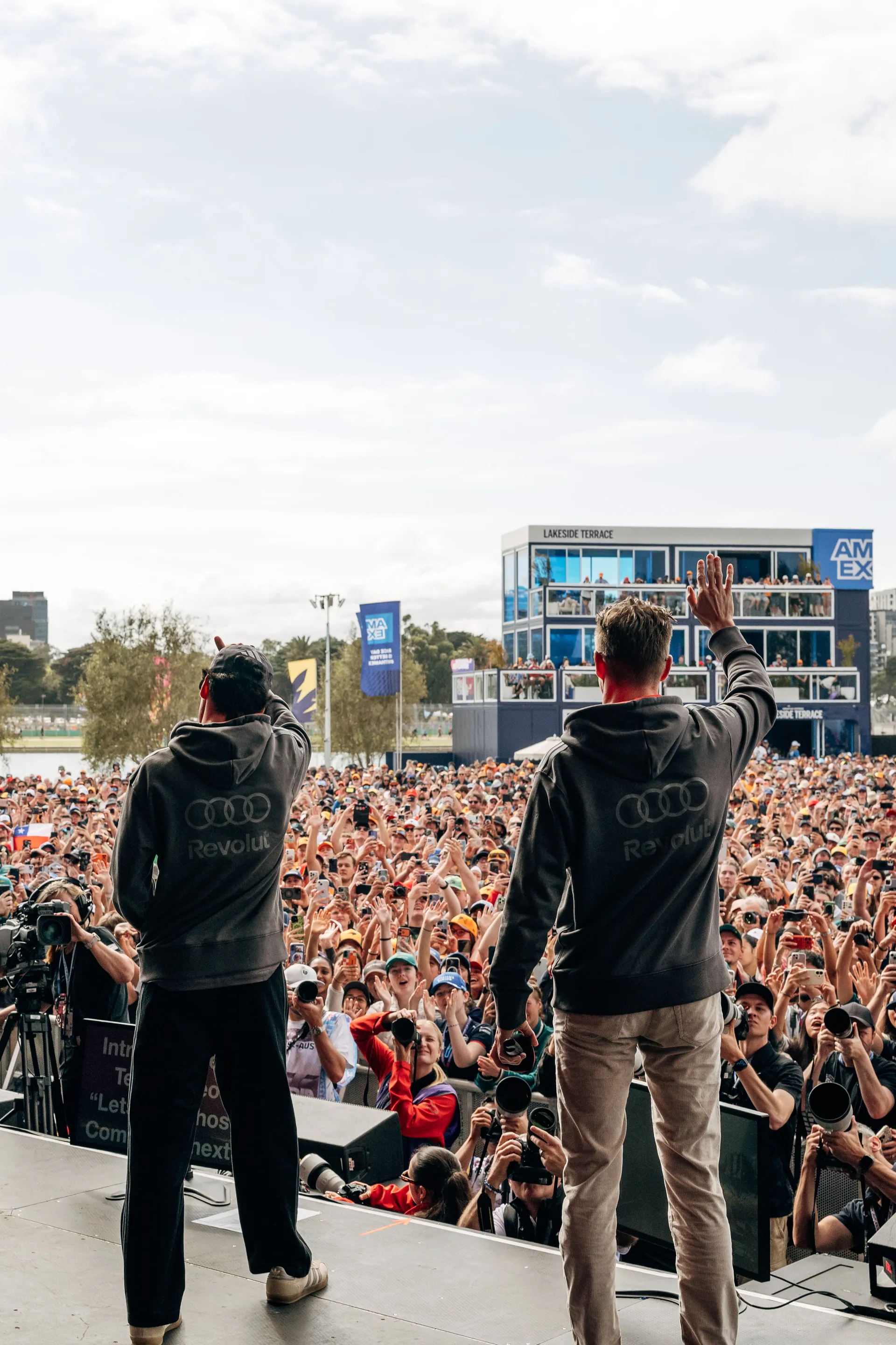 Rear view of Audi Revolut F1® Team drivers Niko Hulkenberg and Gabriel Bortoleto greeting thousands of fans from the stage at a Melbourne Formula 1 event.